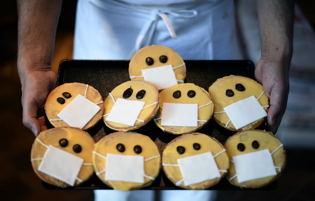 A baker presents biscuits featuring a face with a face mask at the bakery Schuerener Backparadies in Dortmund, western Germany, on March 26, 2020 amidst the spread of the novel coronavirus COVID-19. - The bakery of owner Tim Kortuem sells toilet paper cakes, which are spread with cream and wrapped in fondant. The sweet toilet paper rolls have become a 'bestseller' during the Corona crisis. (Photo by Ina FASSBENDER / AFP)