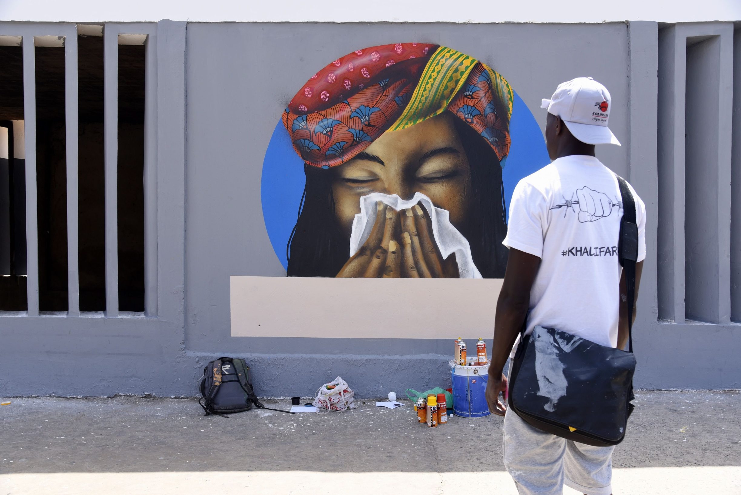 A member of the Senegalese graffitti collective RBS CREW, observes a graffitti representing a woman sneezing in a tissue as a preventive measure against the COVID-19 Coronavirus, tagged on a wall of the Centre des Oeuvres Universitaire(COUD), a university service centre, of the Cheikh Anta Diop University in Dakar on March 21, 2020. - African countries have been among the last to be hit by the global COVID-19 coronavirus epidemic but as cases rise, many nations are now taking strict measures to block the deadly illness. (Photo by Seyllou / AFP)