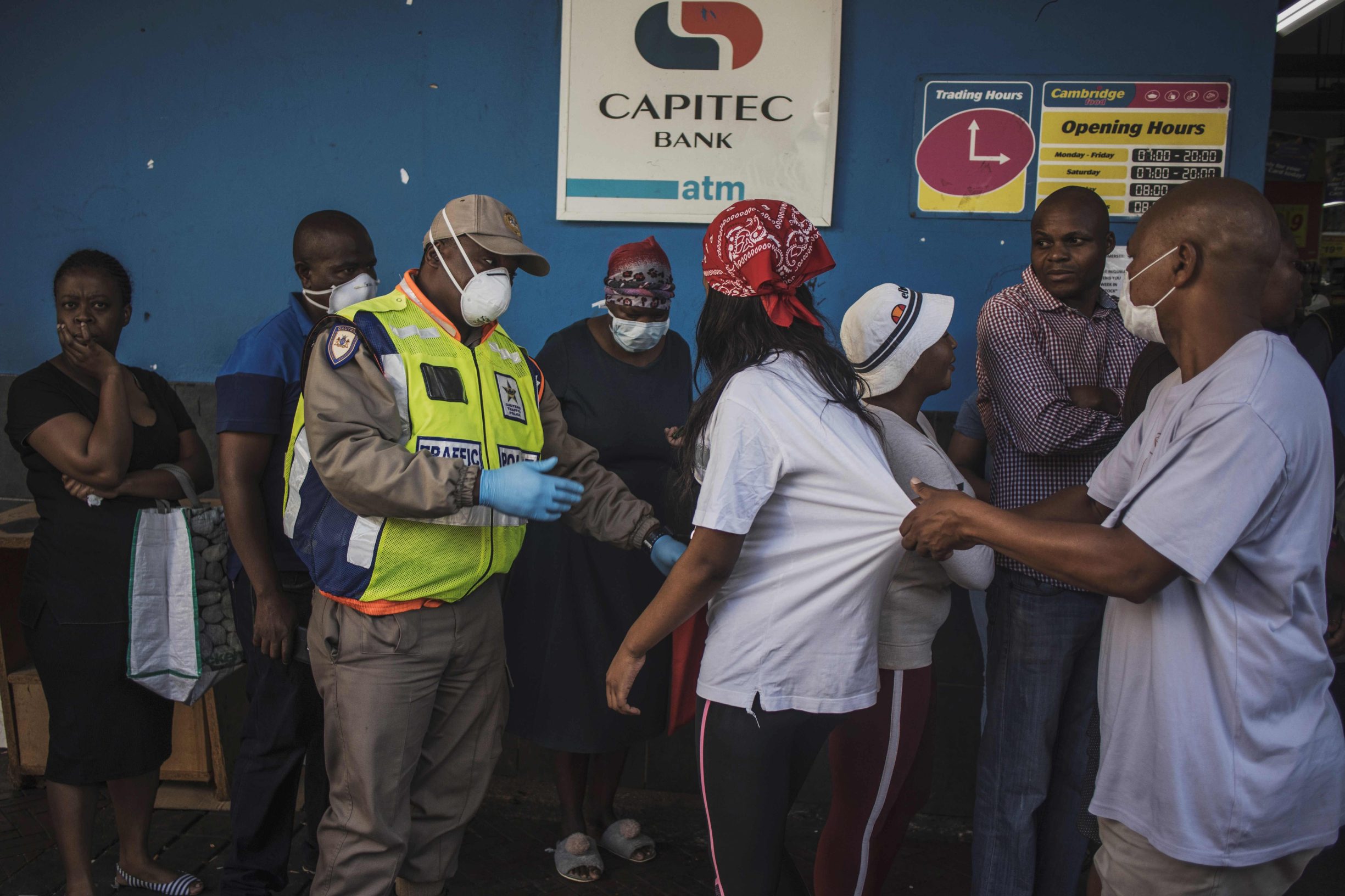 A South African uniformed Metro policeman (L) and a plainclothes one (R) try to enforce distancing outside a supermarket in Hillbrow, Johannesburg, on March 27, 2020 where several dozens of customers are queuing for food without respecting the minimum safety distance. - South Africa came under a nationwide lockdown on March 27, 2020, joining other African countries imposing strict curfews and shutdowns in an attempt to halt the spread of the COVID-19 coronavirus across the continent. (Photo by MARCO LONGARI / AFP)