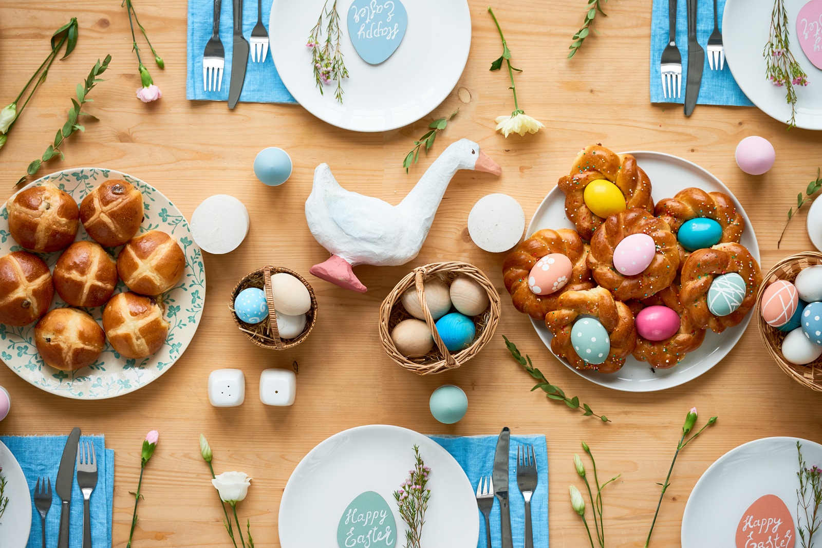 High angle view of picturesque Easter table: painted eggs in small baskets, freshly baked buns on plates and paper-mache goose at center