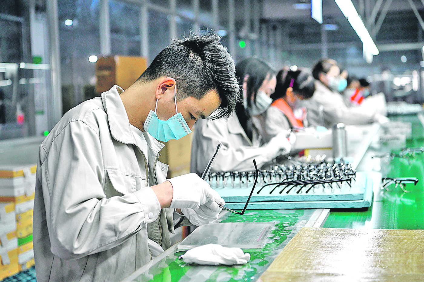 (FILES) This file photo taken on February 28, 2020 shows workers wearing facemasks polishing eyeglass frames at the Azure Eyeglasses Company in Wenzhou. - China's coronavirus epidemic turned a Lunar New Year family reunion into an endless quarantine for factory worker Hu Aihua, preventing him from returning to work in another province. (Photo by NOEL CELIS / AFP) / TO GO WITH HEALTH-VIRUS-CHINA-ECONOMY-EMPLOYMENT BY BEIYI SEOW