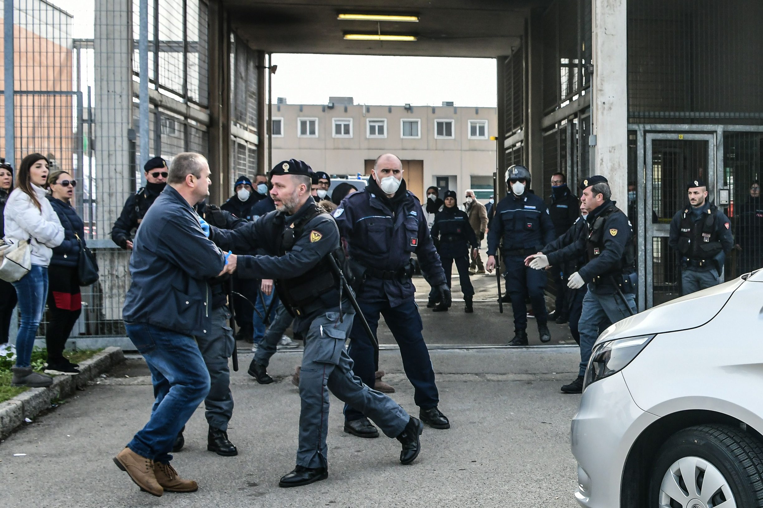 A Police officers holds off an inmate's relative (L) protesting outside the SantAnna prison in Modena, Emilia-Romagna, in one of Italy's quarantine red zones on March 9, 2020. - Inmates in four Italian prisons have revolted over new rules introduced to contain the coronavirus outbreak, leaving one prisoner dead and others injured, a prison rights group said on March 8. Prisoners at jails in Naples Poggioreale in the south, Modena in the north, Frosinone in central Italy and at Alexandria in the northwest had all revolted over measures including a ban on family visits, unions said. (Photo by Piero CRUCIATTI / AFP)