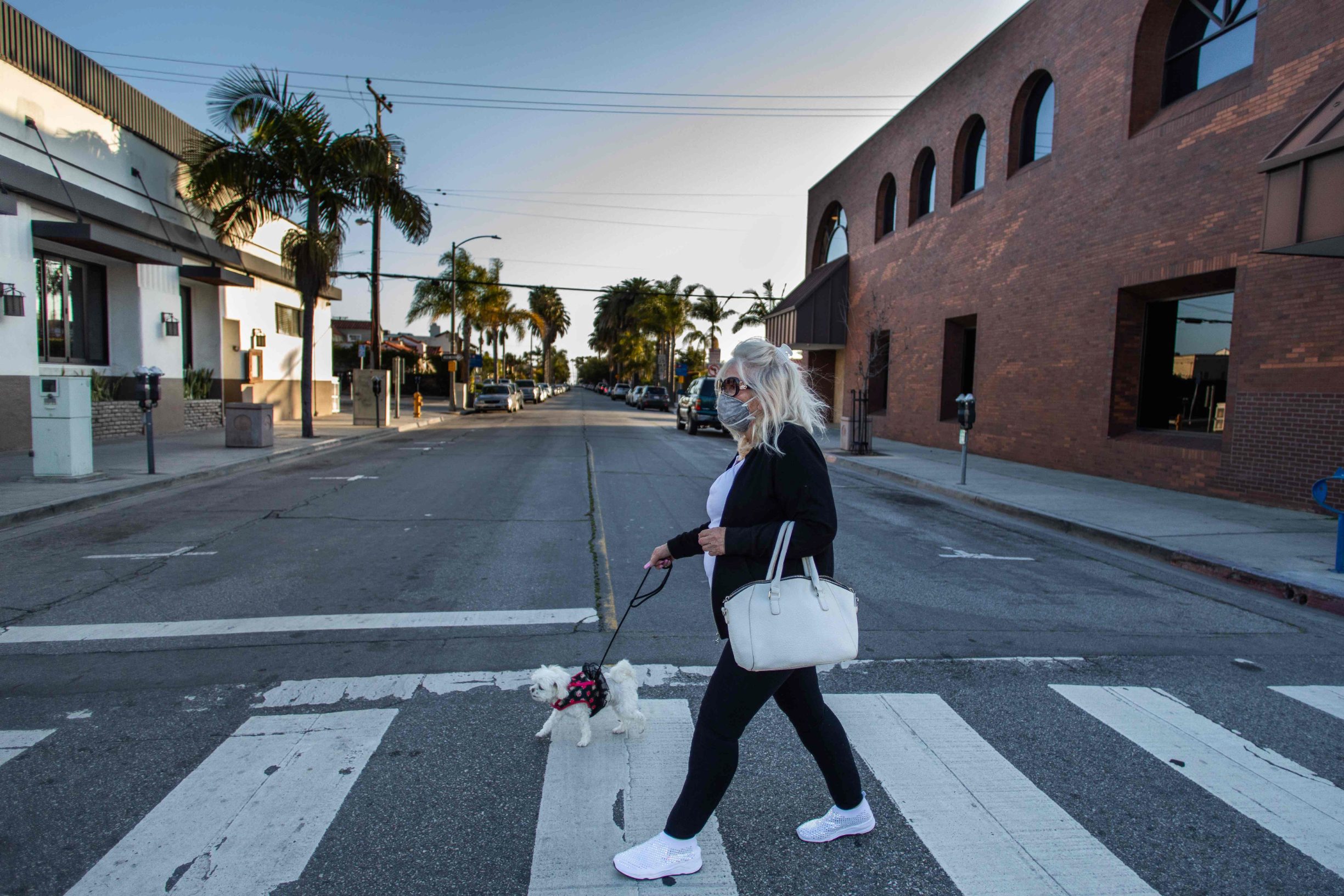 A woman cross the street with her dog in Long Beach, California on March 29, 2020. - President Donald Trump on March 29, 2020, abandoned his timetable for life returning to normal in the United States, extending emergency coronavirus restrictions for another month, while Spain suffered its deadliest day. (Photo by Apu GOMES / AFP)