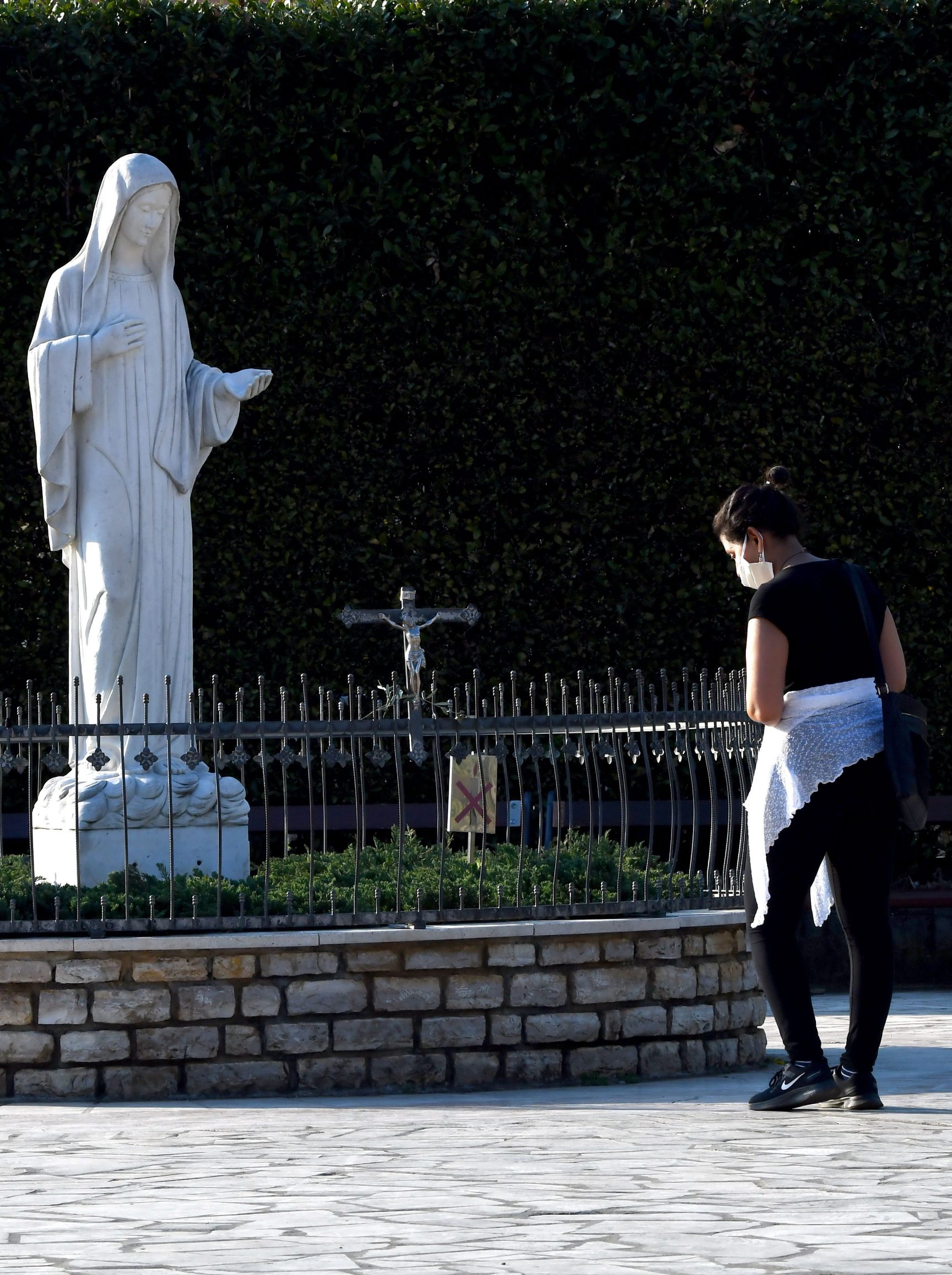 A woman prays next to a Virgin Mary sculpture, in front of the St Jacob church, usually riddled with thousands of Catholic believers, at Marian pilgrimage site, in the southern Bosnian town of Medjugorje, on April 7, 2020 during a lockdown to stop the spread of COVID-19 (novel coronavirus). - Ever since the Virgin Mary was said to appear before six teenagers on a hill in Bosnia four decades ago, pilgrims have flocked to the town of Medjugorje, eager to witness a miracle. (Photo by ELVIS BARUKCIC / AFP)