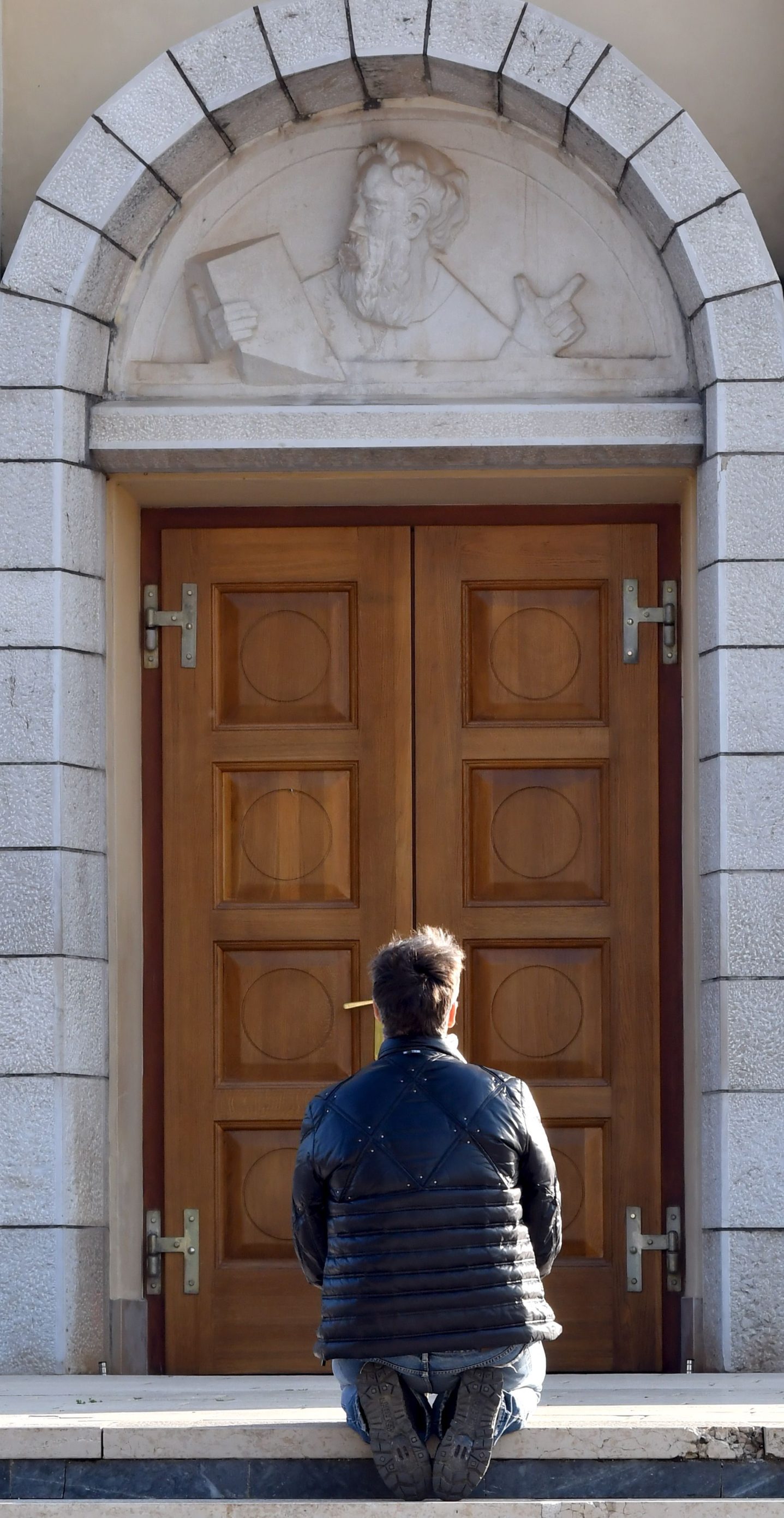 A man prays alone on the doorstep of the St Jacob church, usually riddled with thousands of Catholic believers, at Marian pilgrimage site, in the southern Bosnian town of Medjugorje, on April 7, 2020 during a lockdown to stop the spread of COVID-19 (novel coronavirus). - Ever since the Virgin Mary was said to appear before six teenagers on a hill in Bosnia four decades ago, pilgrims have flocked to the town of Medjugorje, eager to witness a miracle. (Photo by ELVIS BARUKCIC / AFP)