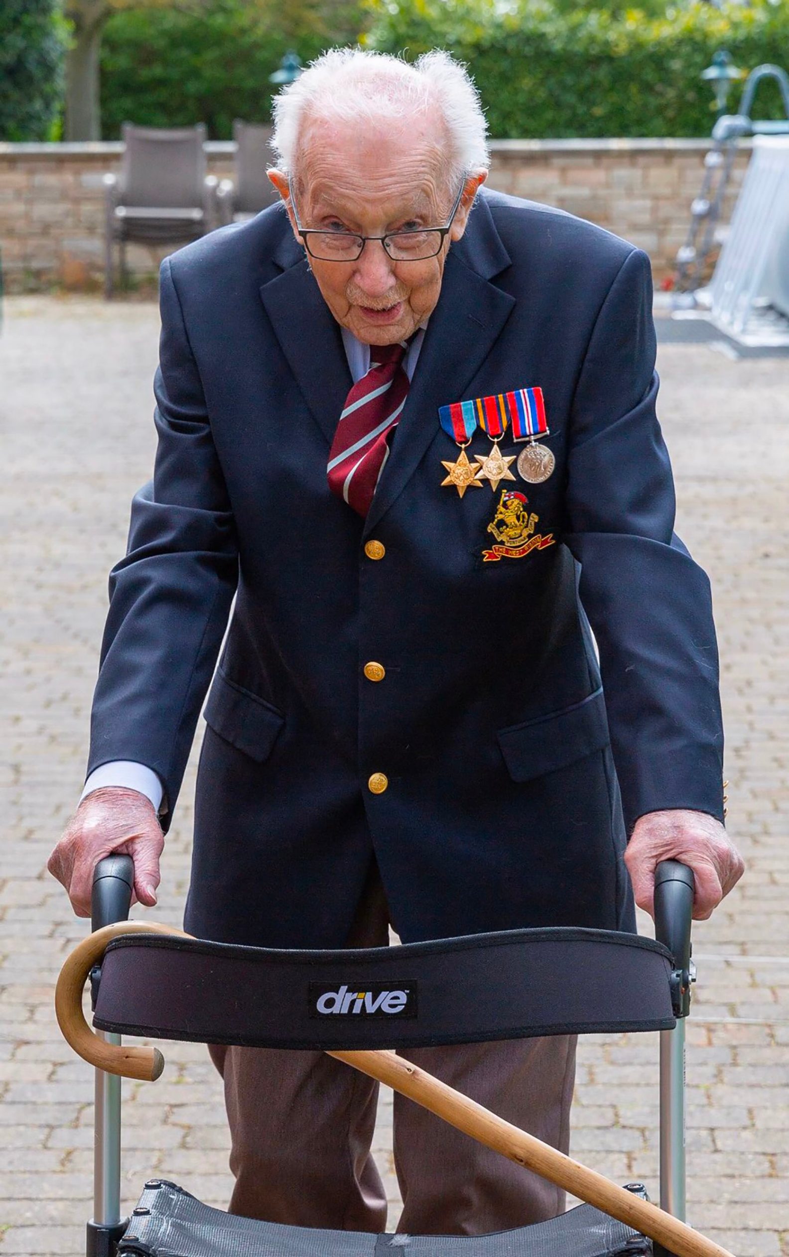 A handout photo taken in April 2020, and released by the Maytrix Group in London on April 14, 2020, shows World War Two (WWII) veteran 99-year-old Captain Tom Moore walking in his garden in Marston Moretaine, north of London, to raise money for Britain's National Health Service (NHS). - A 99-year-old British World War II veteran on Tuesday had raised over £1.5 million (.9 million) for health workers on the coronavirus front-line, crashing the donation website hosting his appeal. Tom Moore, a captain who served in India, is being sponsored to complete 100 lengths of his 25-metre garden, with the aid of a frame, in time for his 100th birthday at the end of the month. He originally planned to raise £1,000 for a National Health Service charity after receiving treatment for a broken hip and cancer. But he has now smashed the million mark and completed 70 laps of his garden in Bedfordshire, south England. (Photo by - / MAYTRIX GROUP / AFP) / RESTRICTED TO EDITORIAL USE - MANDATORY CREDIT 