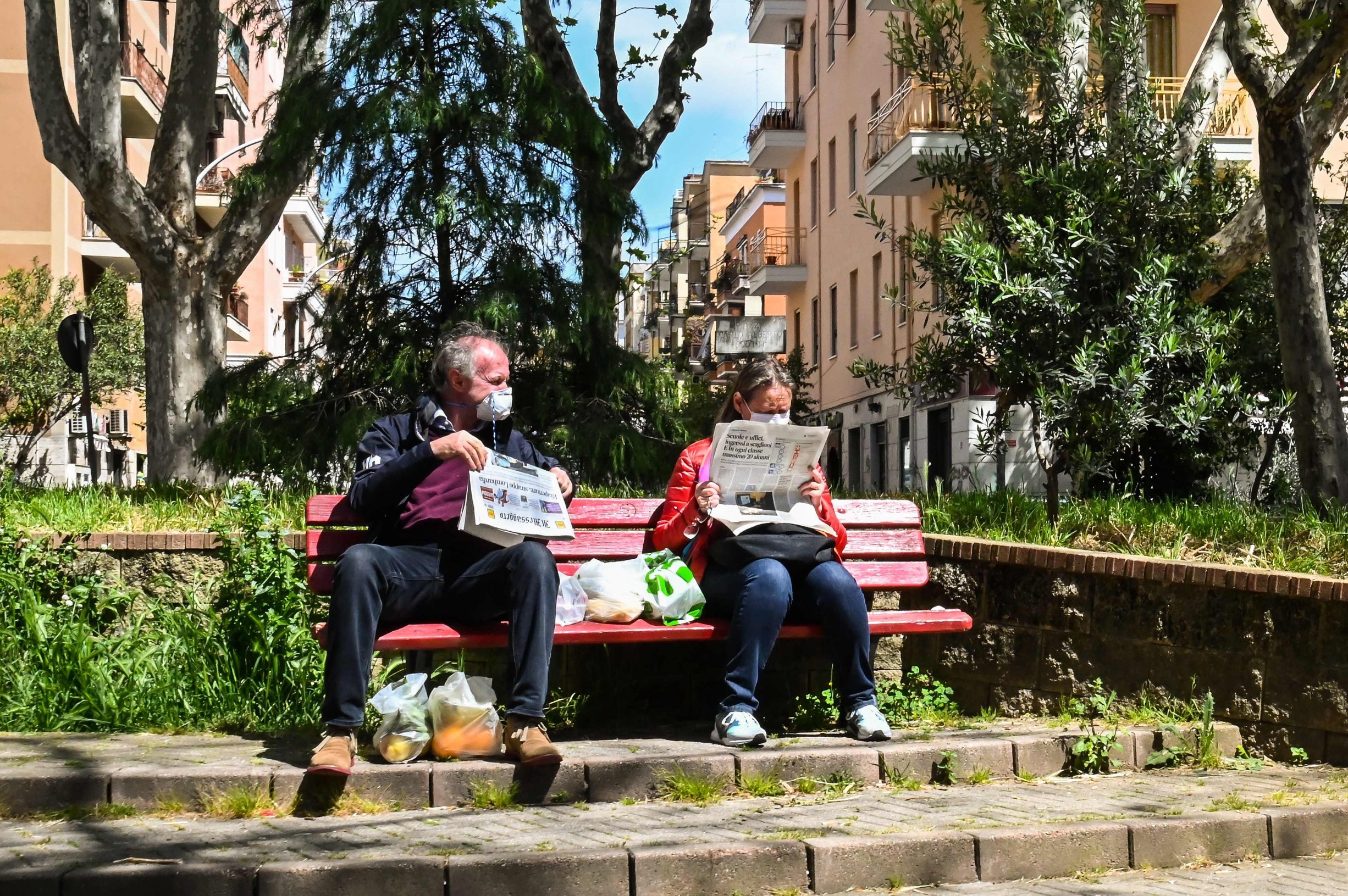 TOPSHOT - People wearing protective masks, read the newspaper as they sit in a square in the district of Monteverde Nuovo in Rome on April 16, 2020, as the nation tries to curb the spread of the COVID-19 epidemic caused by the new coronavirus. (Photo by Andreas SOLARO / AFP)