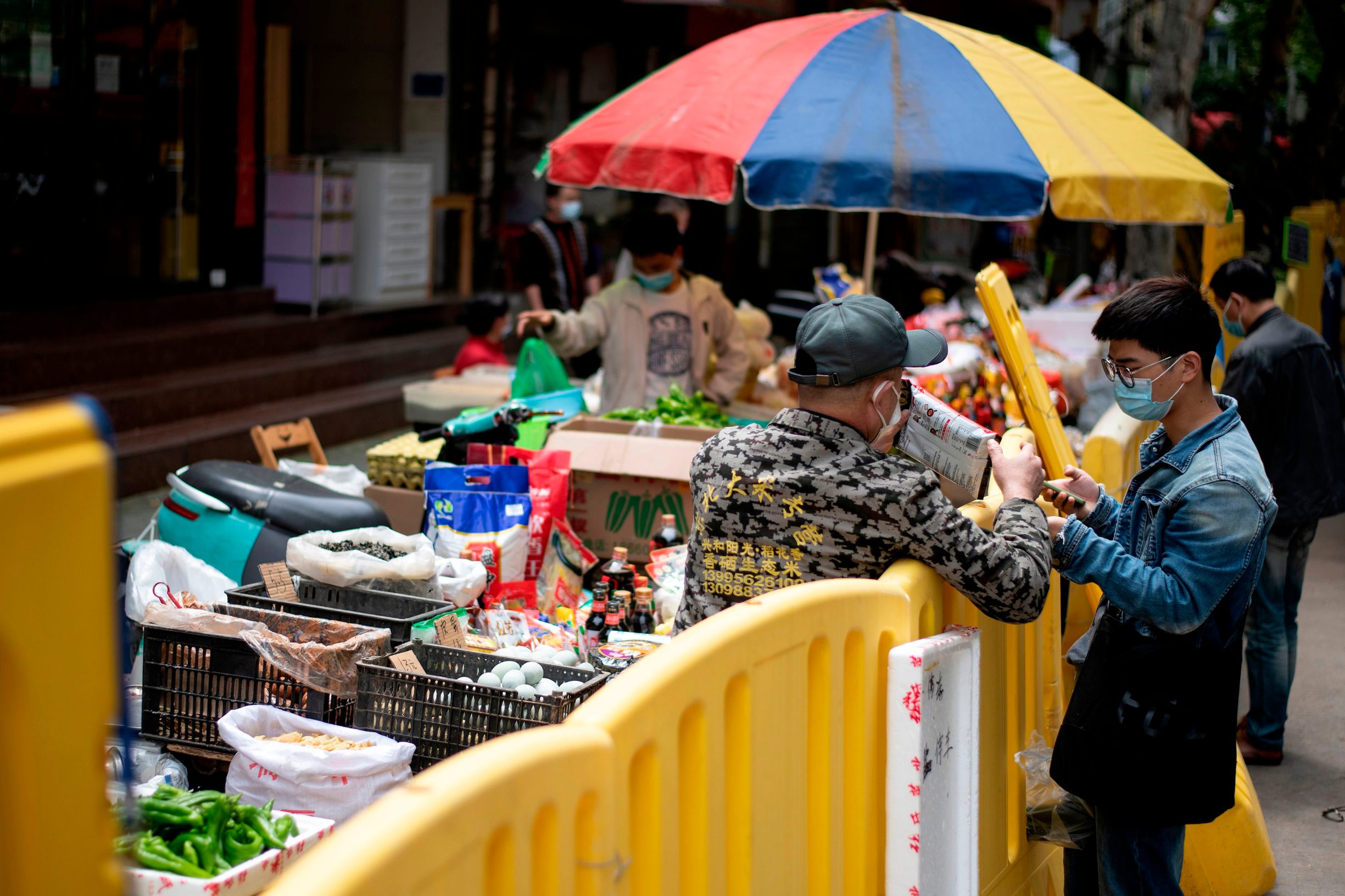 A man (R) wearing a face mask buys goods from a vendor on the other side of a barricaded residential compound in Wuhan in China's central Hubei province on April 14, 2020. (Photo by NOEL CELIS / AFP)