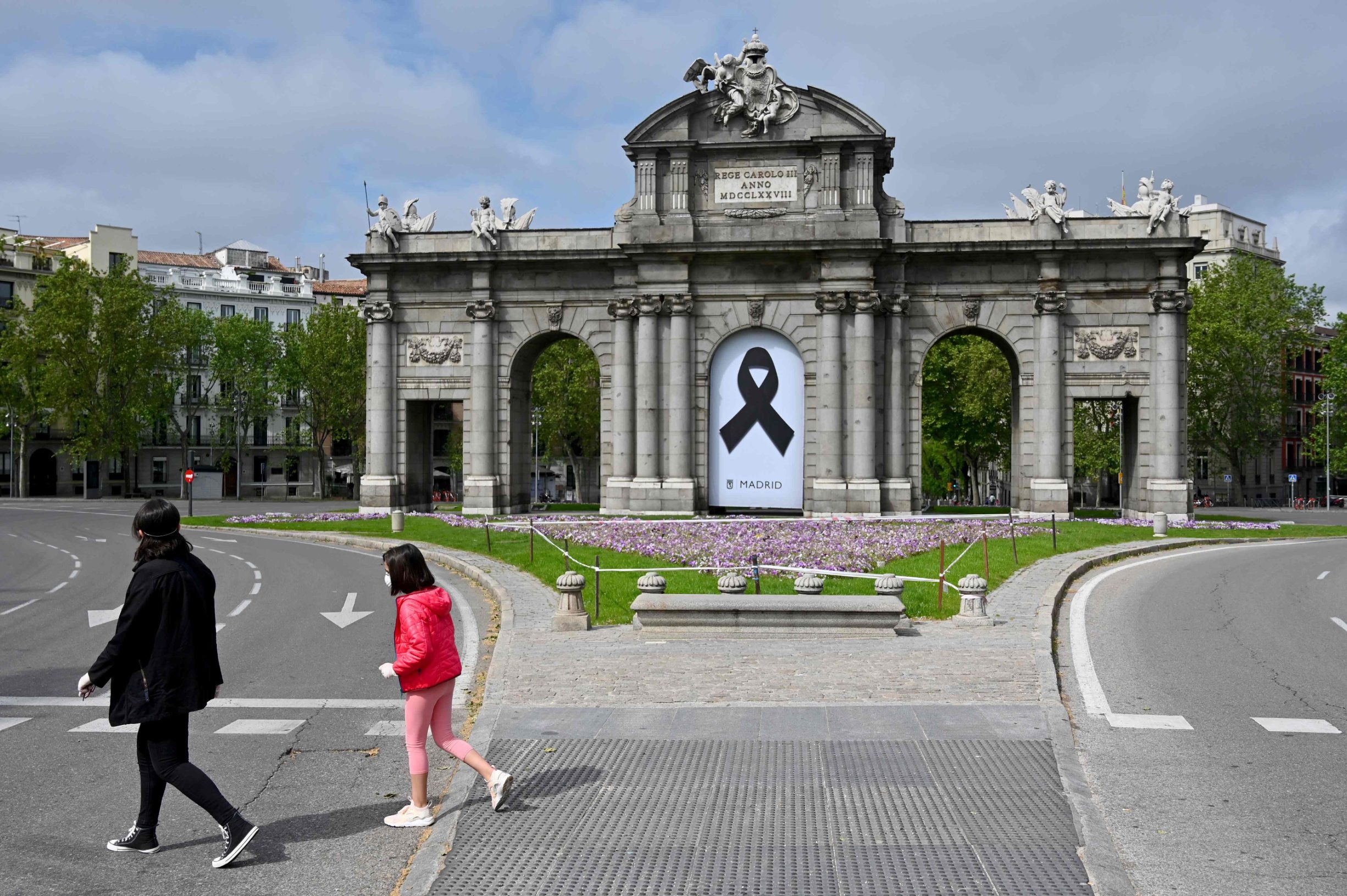 A woman walks with a young girl in front of the Puerta de Alcala monument in Madrid, on April 26, 2020 during a national lockdown to prevent the spread of the COVID-19 disease. - After six weeks stuck at home, Spain's children were being allowed out today to run, play or go for a walk as the government eased one of the world's toughest coronavirus lockdowns. Spain is one of the hardest hit countries, with a death toll running a more than 23,000 to put it behind only the United States and Italy despite stringent restrictions imposed from March 14, including keeping all children indoors. Today, with their scooters, tricycles or in prams, the children accompanied by their parents came out onto largely deserted streets. (Photo by Gabriel BOUYS / AFP)