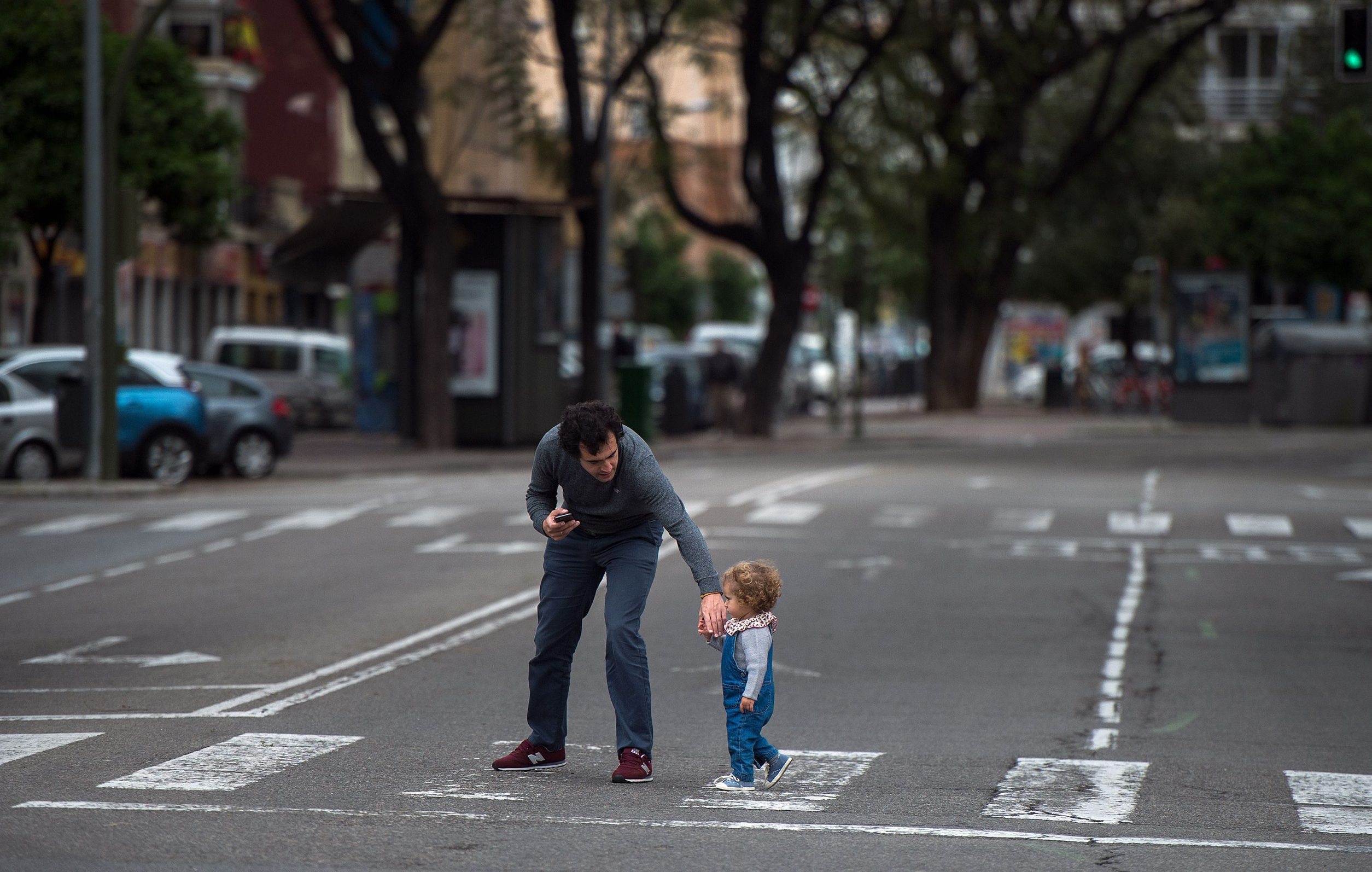 A man crosses a street with a baby in Seville on April 26, 2020 amid a national lockdown to prevent the spread of the COVID-19 disease. - After six weeks stuck at home, Spain's children were being allowed out today to run, play or go for a walk as the government eased one of the world's toughest coronavirus lockdowns. Spain is one of the hardest hit countries, with a death toll running a more than 23,000 to put it behind only the United States and Italy despite stringent restrictions imposed from March 14, including keeping all children indoors. Today, with their scooters, tricycles or in prams, the children accompanied by their parents came out onto largely deserted streets. (Photo by CRISTINA QUICLER / AFP)