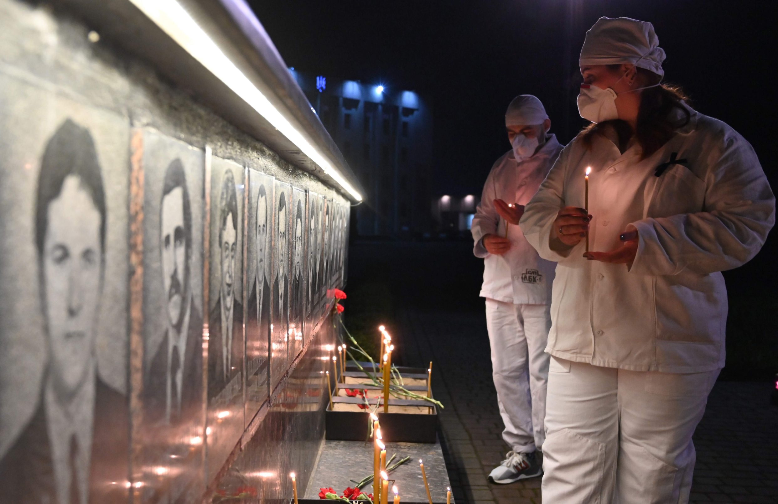 TOPSHOT - Chernobyl plant workers wearing face masks light candles at the monument to Chernobyl victims in Slavutich, the city where the power station's personnel lived, some 50 kilometres (30 miles) from the accident site on April 25, 2020 during a memorial ceremony amid the COVID-19 pandemic, caused by the novel coronavirus. - Ukraine on April 26, 2017 marks the 34th anniversary of the Chernobyl disaster which was the world's worst nuclear accident. (Photo by Sergei SUPINSKY / AFP)