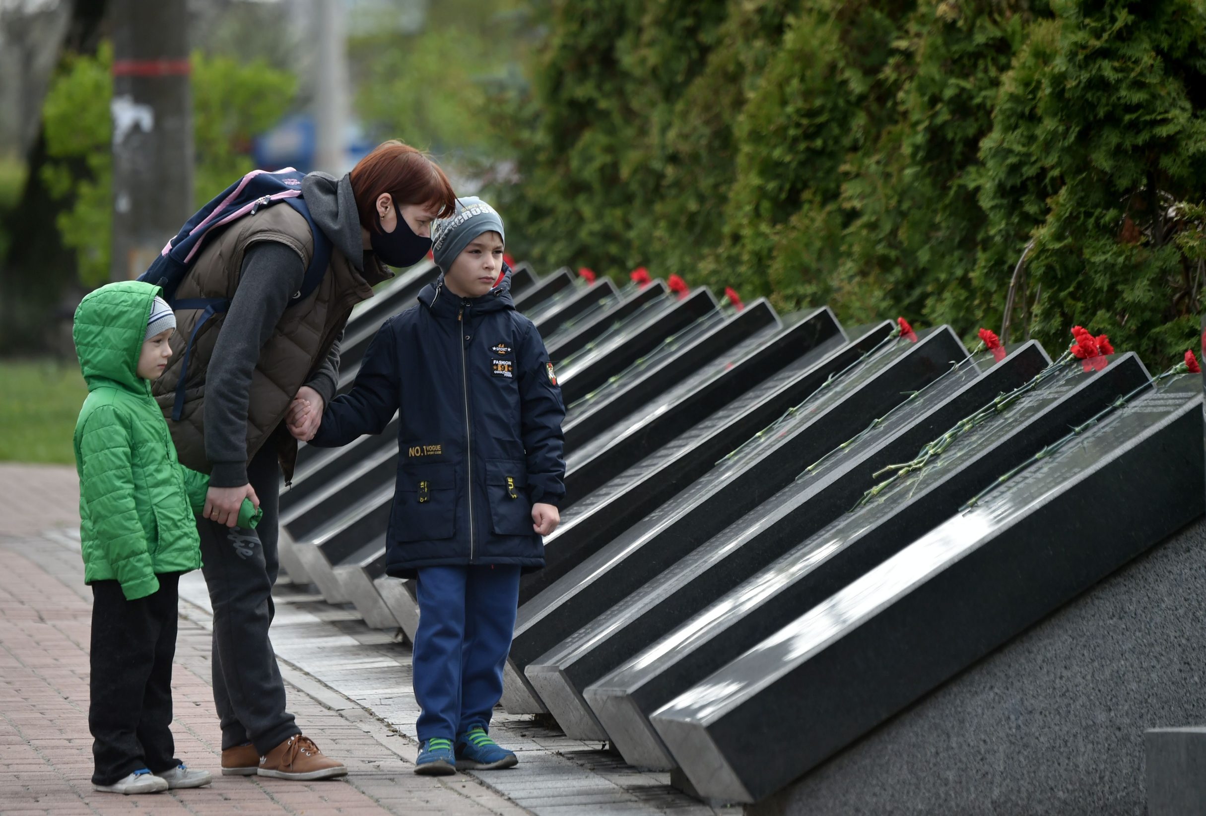 A woman wearing a face mask and her children visit Chernobyl's memorial in Kiev to commemorate the victims on the 34th anniversary of the tragedy on April 26, 2020, amid the COVID-19 coronavirus pandemic. - Ukraine on April 26, 2020 marks the 34th anniversary of the Chernobyl disaster which was the world's worst nuclear accident. (Photo by Sergei SUPINSKY / AFP)