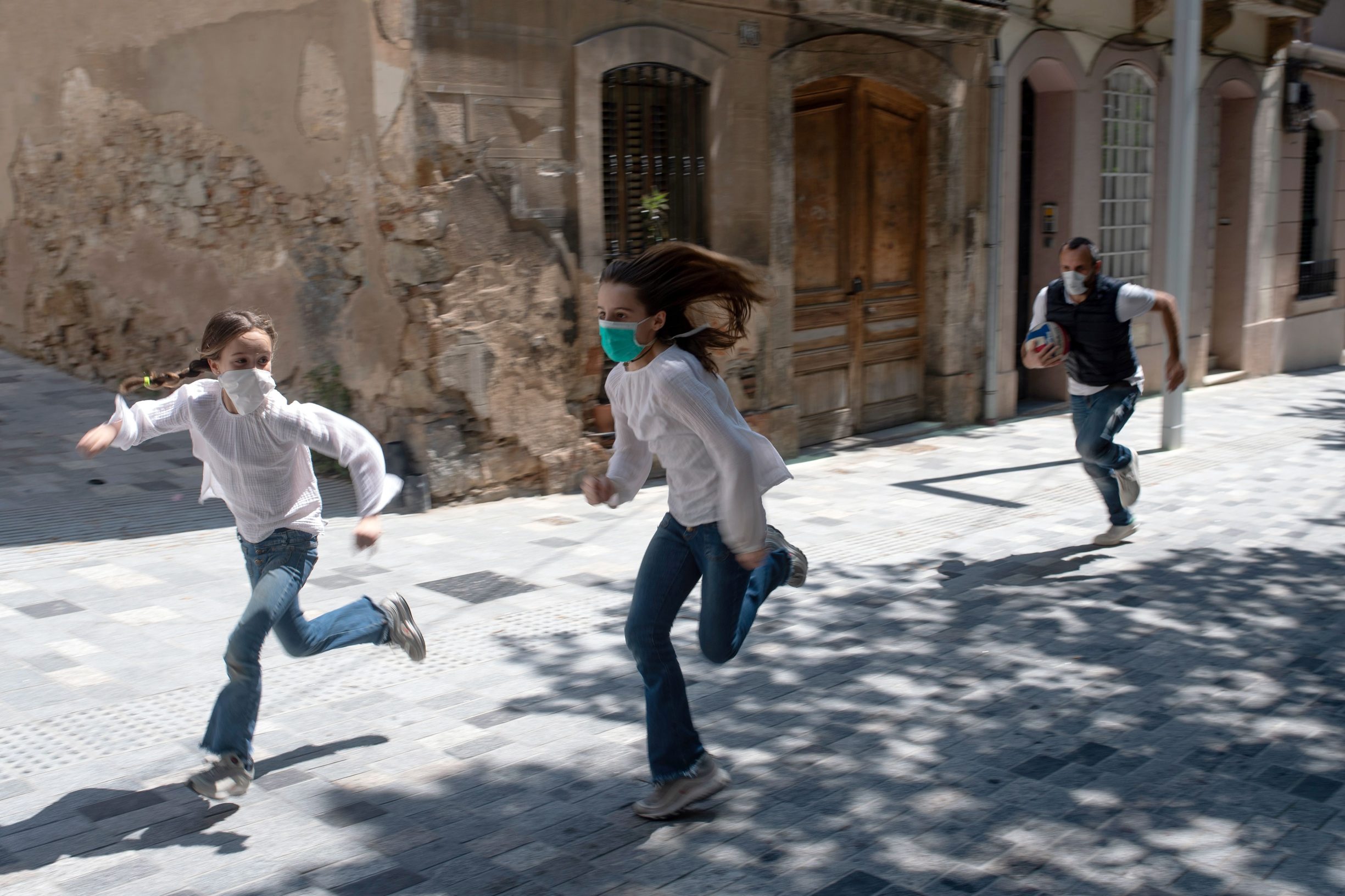 TOPSHOT - Joan, 45, chases his daughters Ines, 11, and Mar, 9, as they play in the street on April 26, 2020, in Barcelona, during a national lockdown to prevent the spread of the COVID-19 disease. - After six weeks stuck at home, Spain's children were being allowed out today to run, play or go for a walk as the government eased one of the world's toughest coronavirus lockdowns. Spain is one of the hardest hit countries, with a death toll running a more than 23,000 to put it behind only the United States and Italy despite stringent restrictions imposed from March 14, including keeping all children indoors. Today, with their scooters, tricycles or in prams, the children accompanied by their parents came out onto largely deserted streets. (Photo by Josep LAGO / AFP)