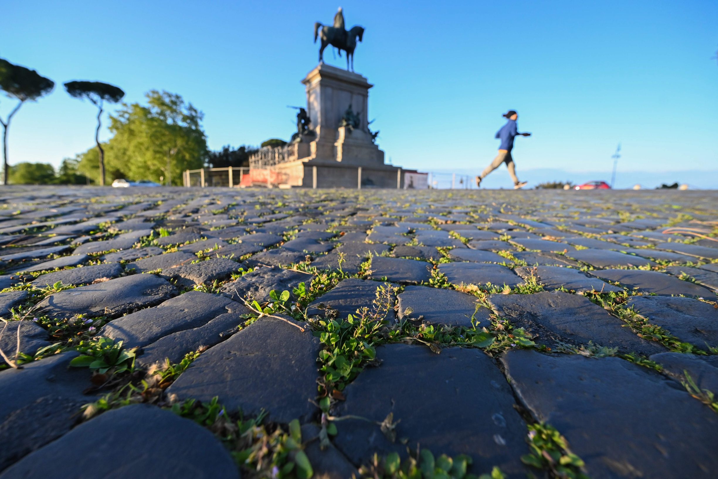 TOPSHOT - Grass grows between the road's cobblestones as a woman jogs past the equestrian statue of Giuseppe Garibaldi on April 26, 2020 at the Gianicolo terrace overlooking Rome, during the country's lockdown aimed at curbing the spread of the COVID-19 infection, caused by the novel coronavirus. (Photo by ANDREAS SOLARO / AFP)