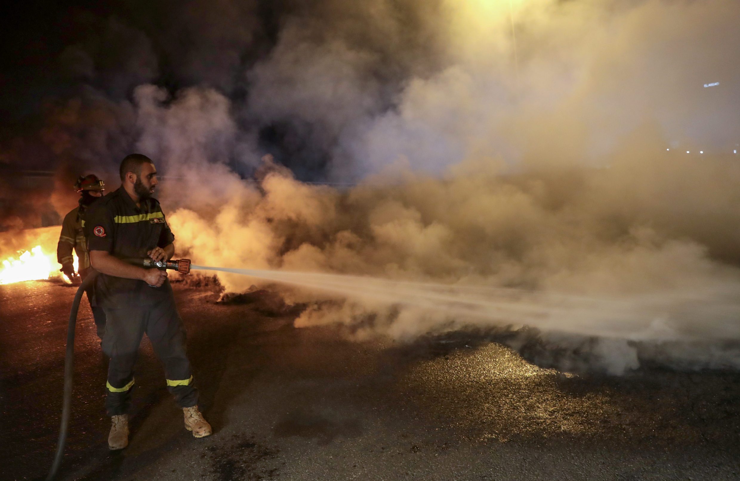 Members of the Lebanese civil defence quell burning tyres which anti-government protesters have set on fire, blocking the coastal highway north in the Dbayeh area, north of the capital Beirut, early on April 27, 2020, in protest of the deteriorating economic situation. - Lebanon's worst economic crisis since the 1975-1990 civil war is now compounded by the coronavirus lockdown and nighttime curfew. Still, protesters have staged several daytime demonstrations recently, in continuation of a nationwide protest which erupted in October last year. (Photo by ANWAR AMRO / AFP)