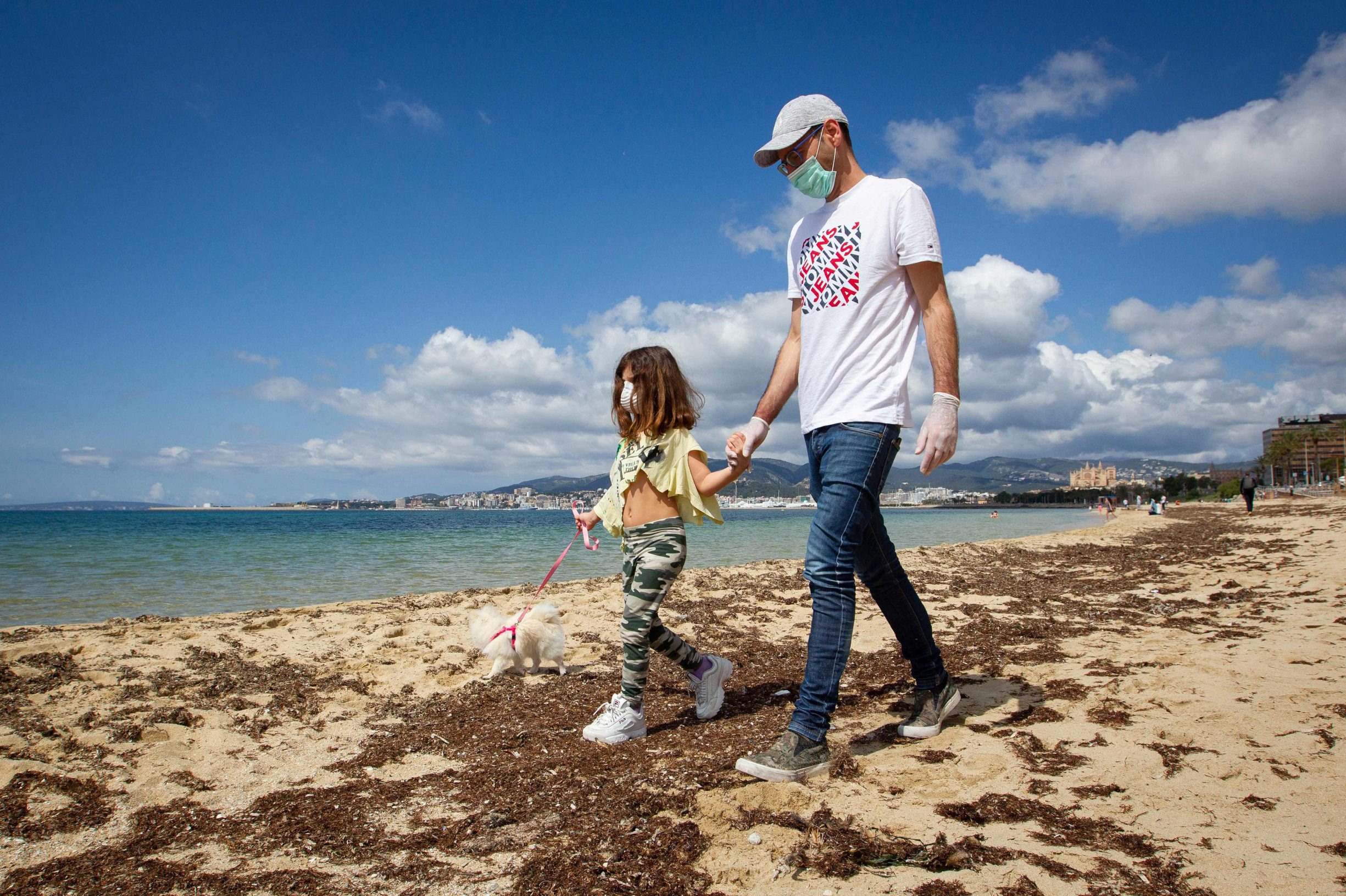 A girls walks her dog with her father on Can Pere Antoni Beach in Palma de Mallorca, on April 26, 2020 during a national lockdown to prevent the spread of the COVID-19 disease. - After six weeks stuck at home, Spain's children were being allowed out today to run, play or go for a walk as the government eased one of the world's toughest coronavirus lockdowns. Spain is one of the hardest hit countries, with a death toll running a more than 23,000 to put it behind only the United States and Italy despite stringent restrictions imposed from March 14, including keeping all children indoors. Today, with their scooters, tricycles or in prams, the children accompanied by their parents came out onto largely deserted streets. (Photo by JAIME REINA / AFP)