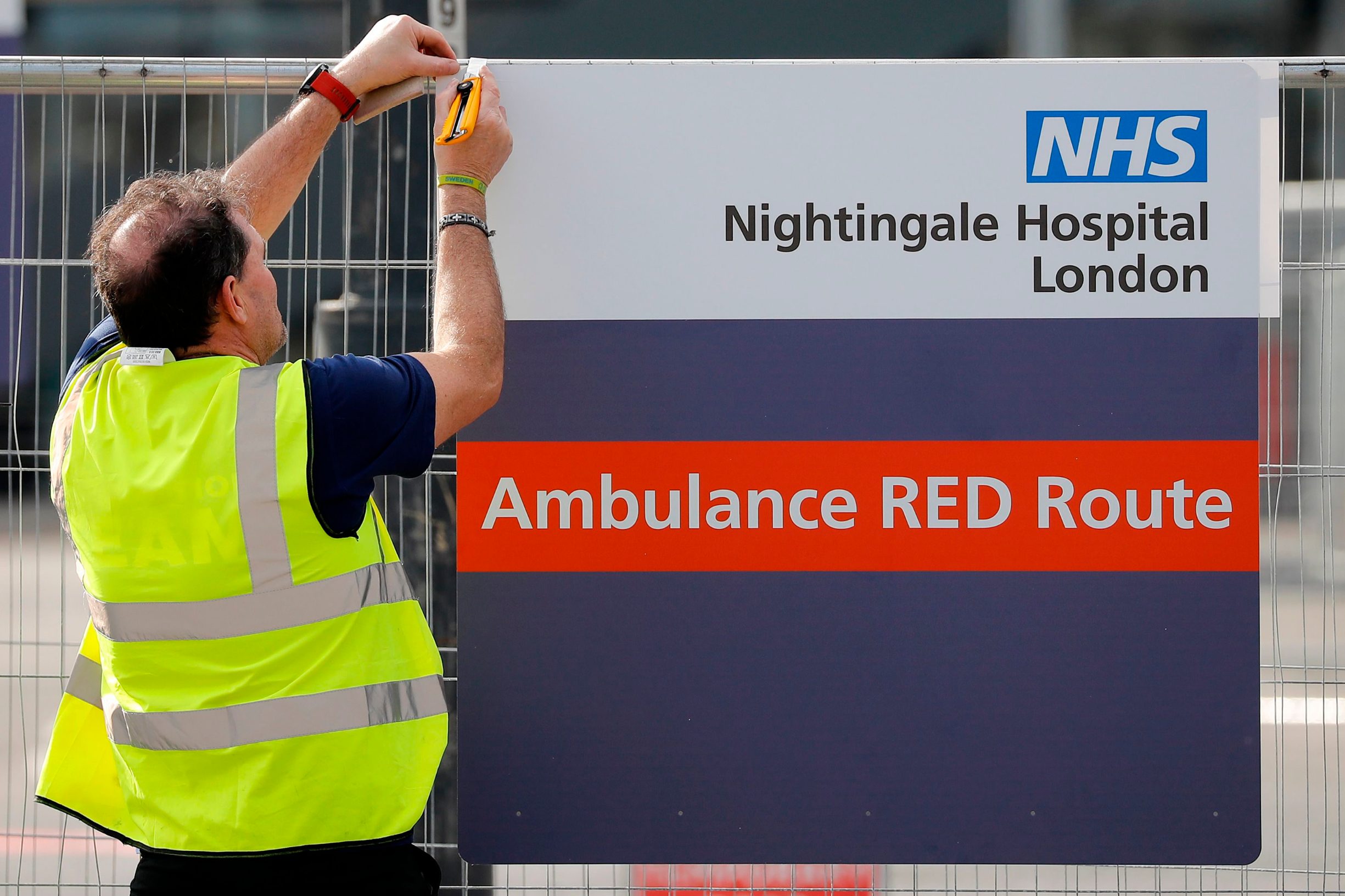 A worker affixes a new sign to a fence at the ExCeL London exhibition centre, which has been transformed into the 