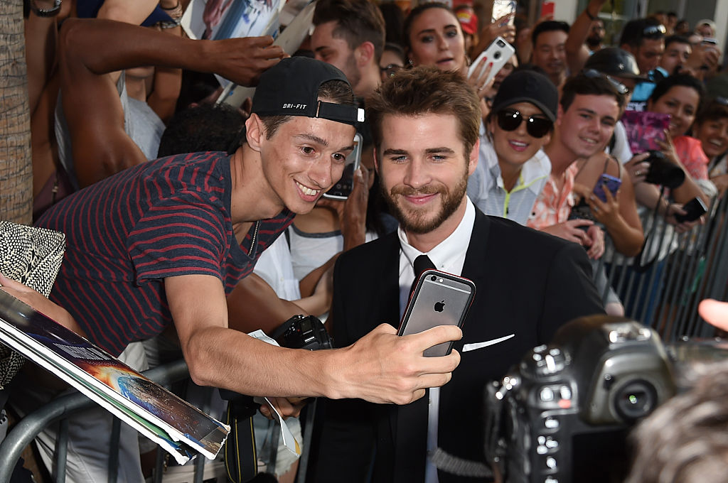 HOLLYWOOD, CA - JUNE 20:  Actor Liam Hemsworth (R) takes a selfie with a fan during the premiere of 20th Century Fox's 