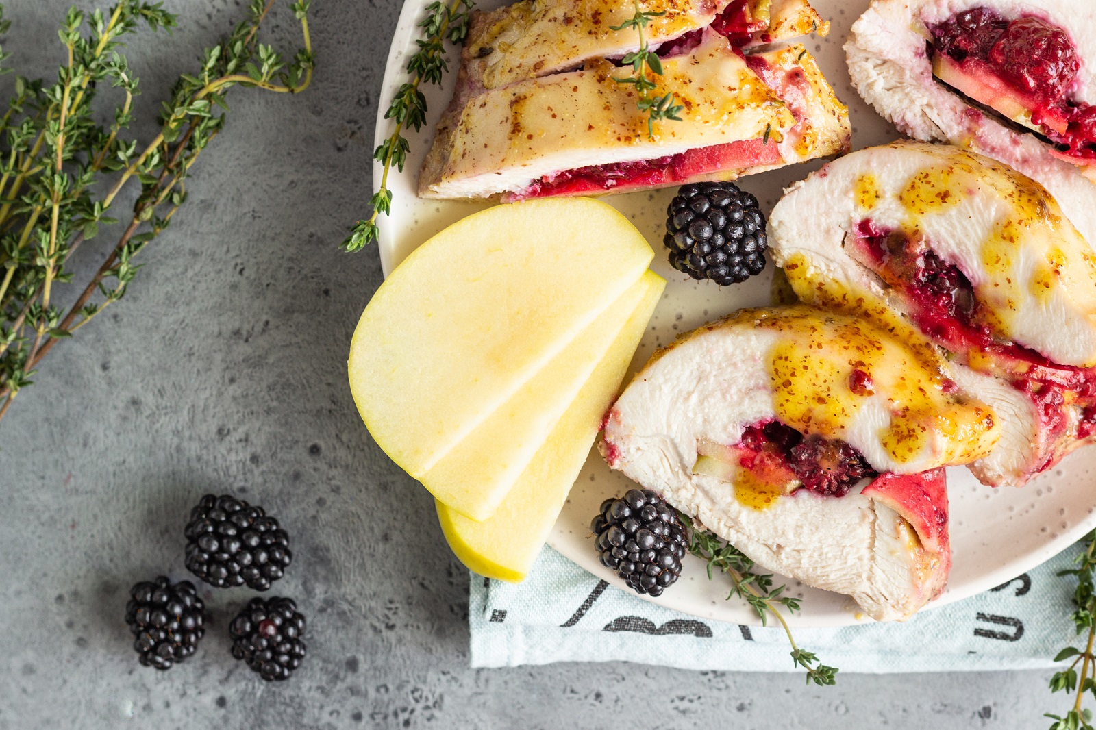 Baked turkey or chicken breast stuffed with apples and blackberries. Light grey background.