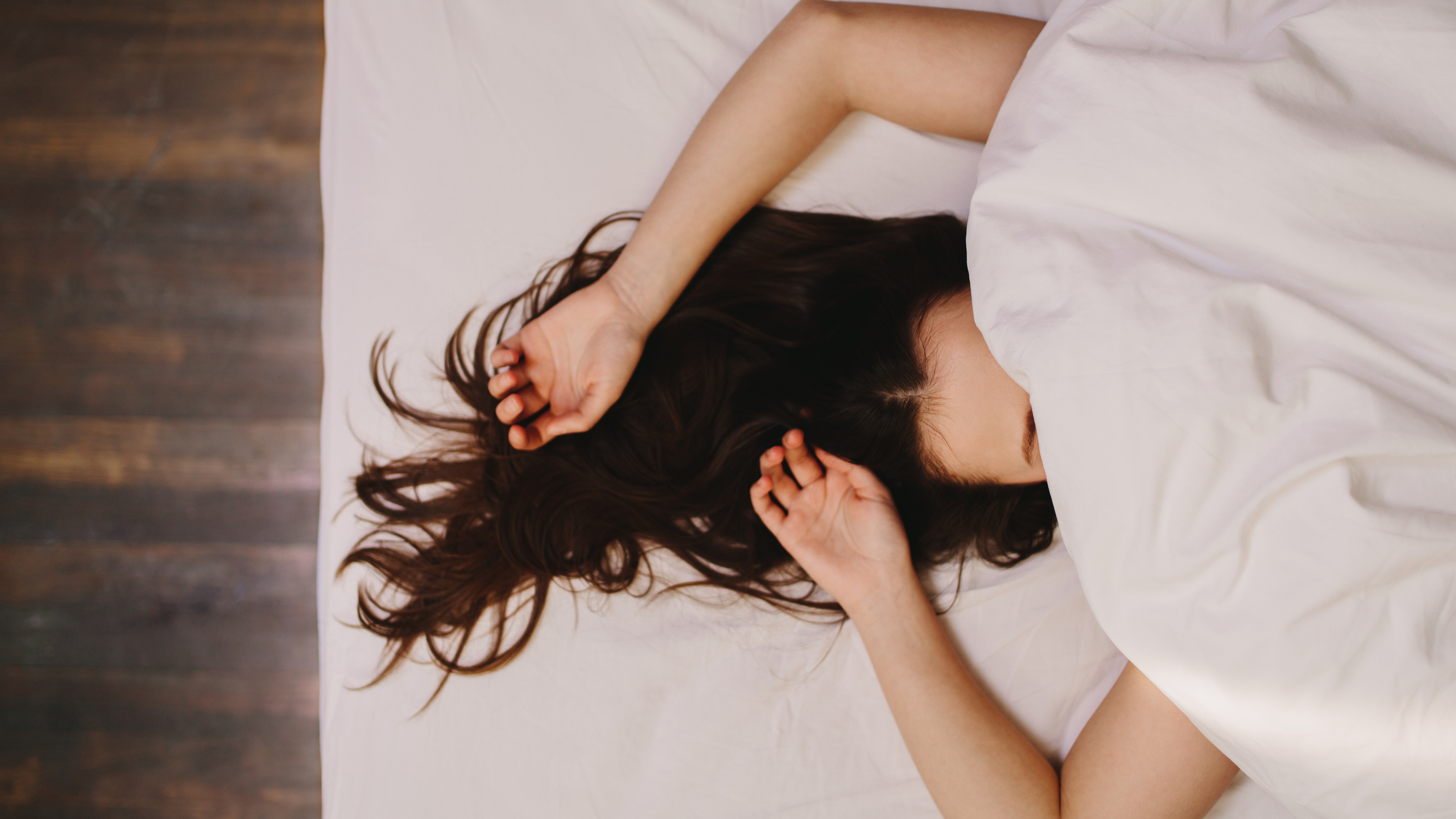 Top view of a woman sleeping on bed covering her face. Close up of a woman in deep sleep with her hand beside her head and hair let loose.