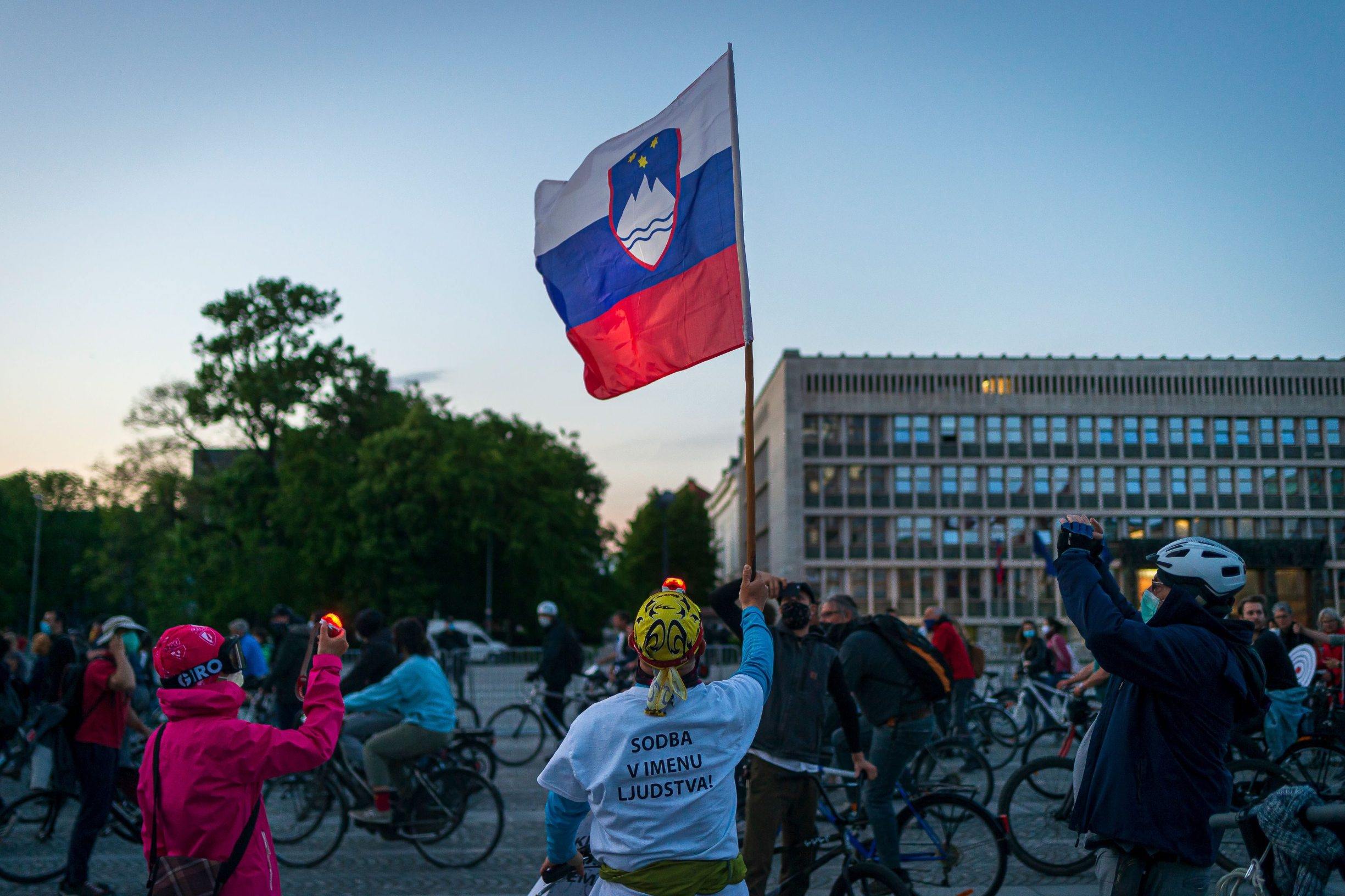 TOPSHOT - A man holds a Slovenian flag as others ride their bikes as they block the centre of capital Ljubljana to protest against the centre-right government, accusing it of corruption and of using the novel coronavirus crisis to restrict freedom on May 8, 2020 amid the COVID-19 outbreak, caused by the novel coronavirus. (Photo by Jure Makovec / AFP)