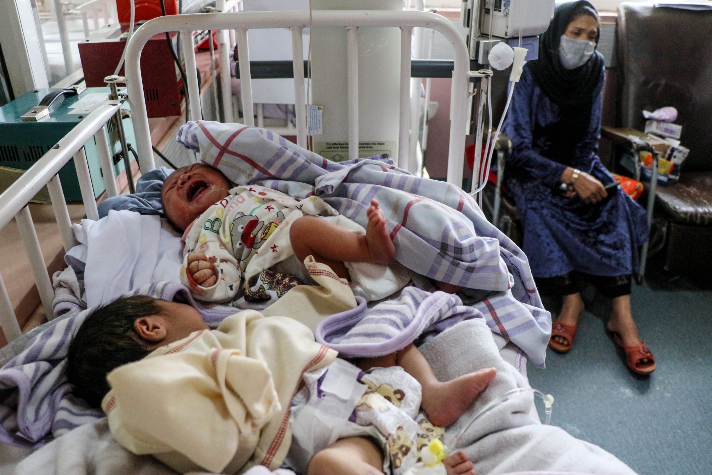 TOPSHOT - A woman (R) sits next to newborn babies who lost their mothers following a suicide attack in a maternity hospital, in Kabul on May 13, 2020. - The combined death toll from two attacks in Afghanistan, including one on a hospital in which infants and nurses were killed, has risen to 56, health officials said May 13. Three gunmen stormed a Kabul maternity hospital on May 12 as parents brought infants and children for appointments. (Photo by STR / AFP)