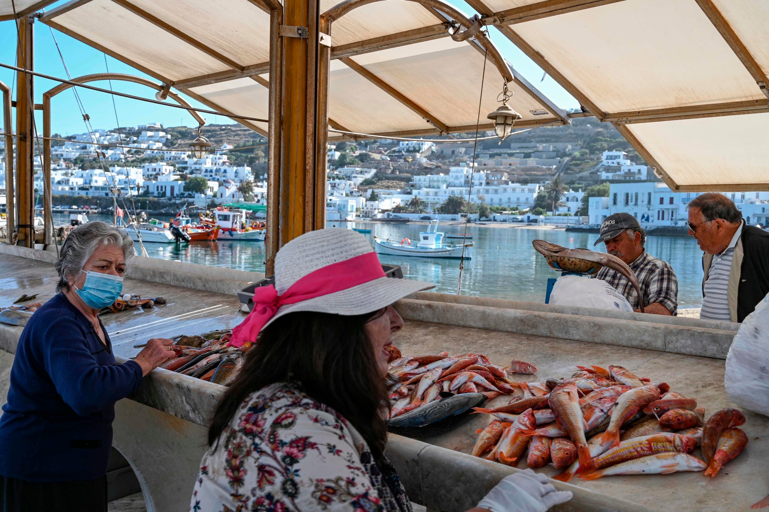 People buy fresh fish at a fisherman stand in the old port of the Greek Cycladic island of Mykonos, on May 13, 2020. - In Mykonos, at the start of the tourist season, the image is striking: the posh island traditionally crowded with wealthy foreigners has turned into a ghost island, offering visitors deserted alleys, boarded up shops, restaurants and abandoned hotels. (Photo by ARIS MESSINIS / AFP)