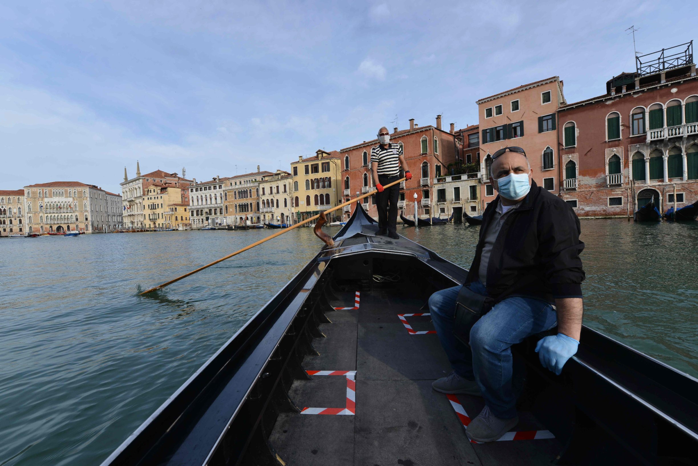 TOPSHOT - A gondolier wearing a face mask (Rear) transports his very first customer as service resumes at the San Toma embankment on a Venice canal on May 18, 2020 during the country's lockdown aimed at curbing the spread of the COVID-19 infection, caused by the novel coronavirus. - Restaurants and churches reopen in Italy on May 18, 2020 as part of a fresh wave of lockdown easing in Europe and the country's latest step in a cautious, gradual return to normality, allowing businesses and churches to reopen after a two-month lockdown. (Photo by ANDREA PATTARO / AFP)