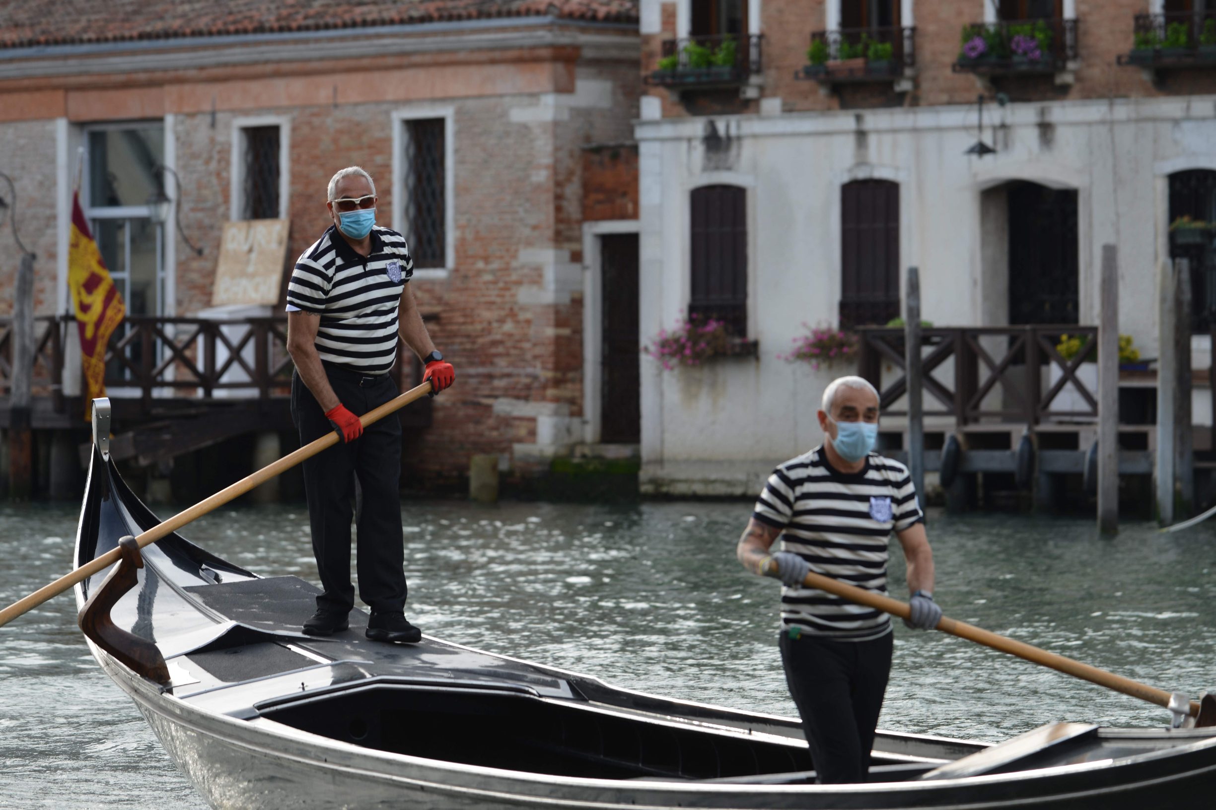 Gondoliers wearing a face mask ride a gondola by the San Toma embankment on a Venice canal as they resume service on May 18, 2020 during the country's lockdown aimed at curbing the spread of the COVID-19 infection, caused by the novel coronavirus. - Restaurants and churches reopen in Italy on May 18, 2020 as part of a fresh wave of lockdown easing in Europe and the country's latest step in a cautious, gradual return to normality, allowing businesses and churches to reopen after a two-month lockdown. (Photo by ANDREA PATTARO / AFP)