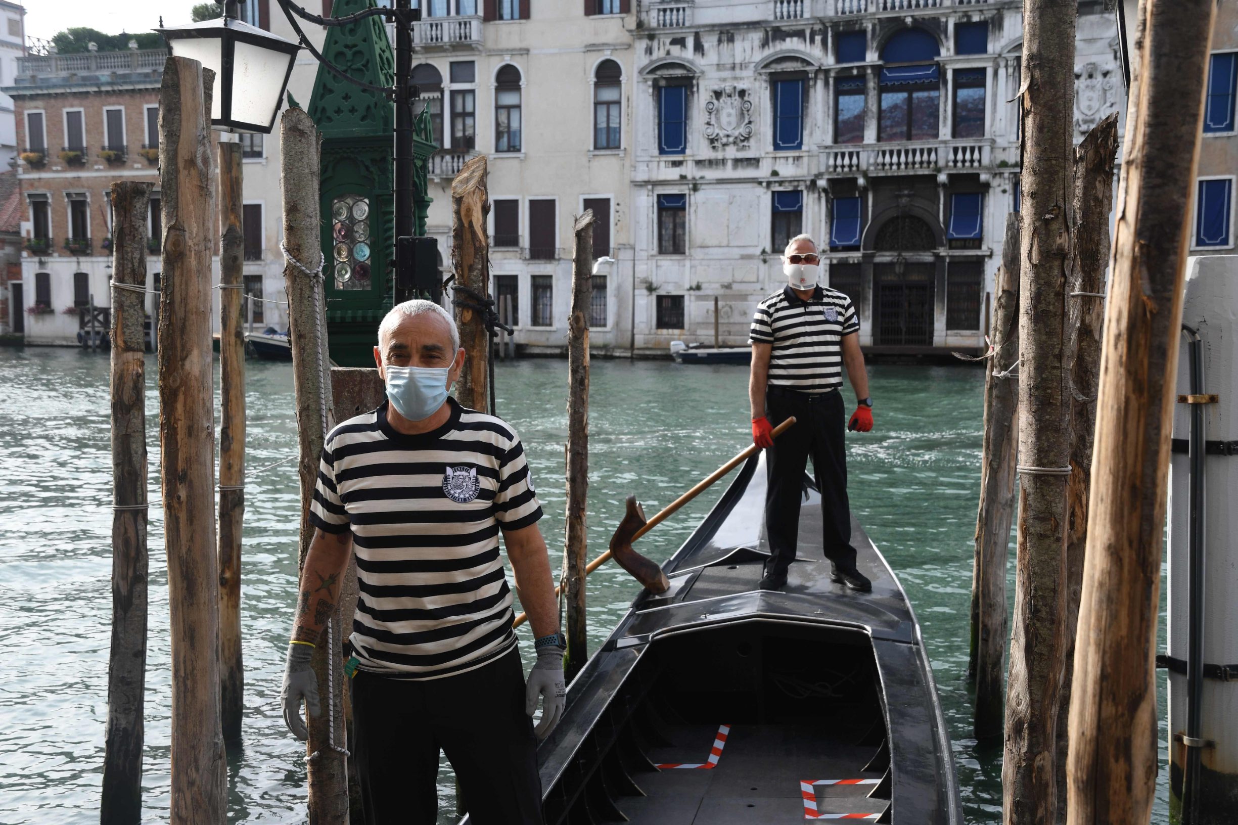 Gondoliers wearing a face mask stand on a gondola on a Venice canal as they resume their service on May 18, 2020 during the country's lockdown aimed at curbing the spread of the COVID-19 infection, caused by the novel coronavirus. - Restaurants and churches reopen in Italy on May 18, 2020 as part of a fresh wave of lockdown easing in Europe and the country's latest step in a cautious, gradual return to normality, allowing businesses and churches to reopen after a two-month lockdown. (Photo by ANDREA PATTARO / AFP)