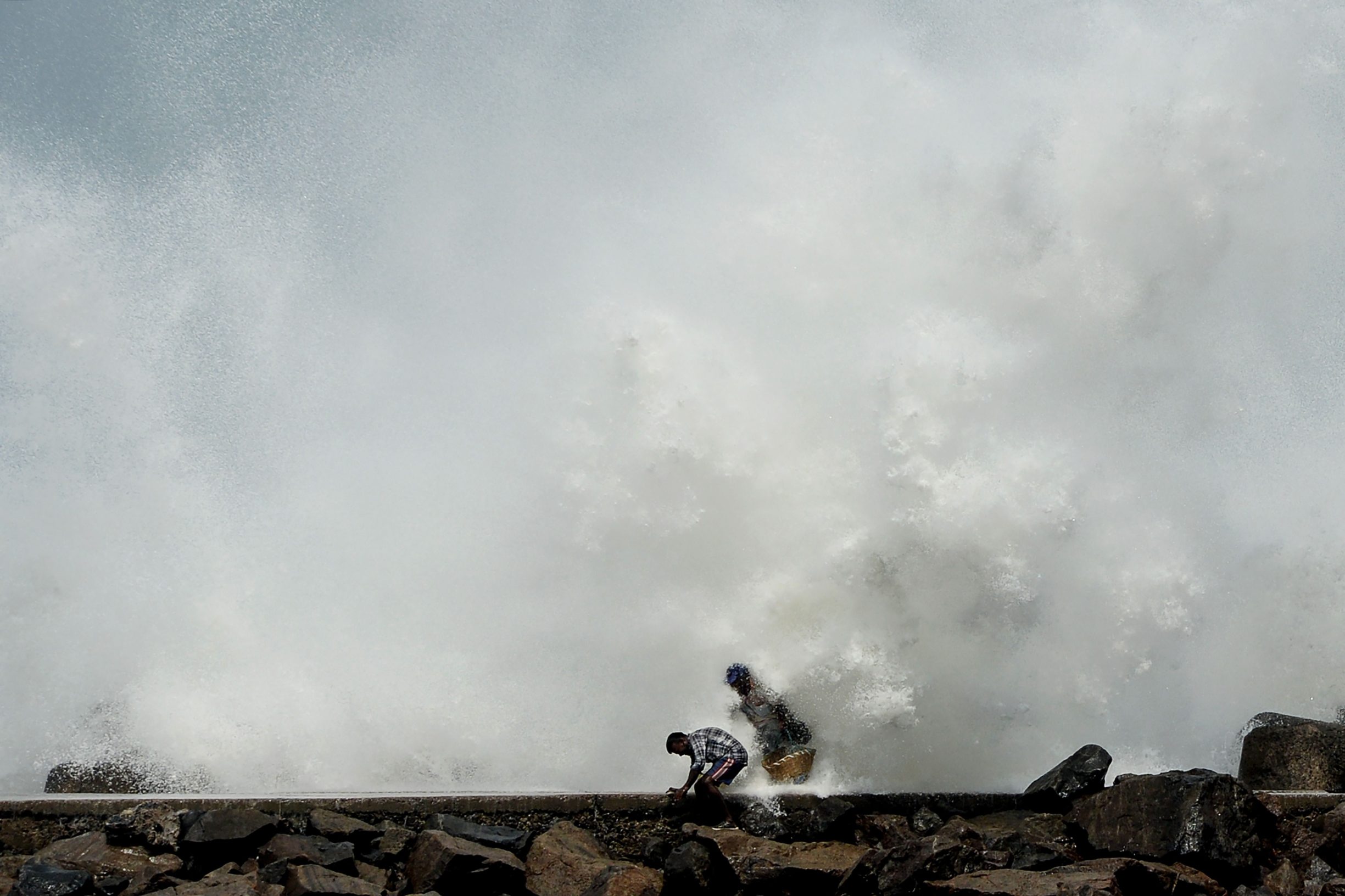 TOPSHOT - Men walk past as waves hit a breakwater at Kasimedu fishing harbour in Chennai on May 19, 2020, as Cyclone Amphan barrels towards India's eastern coast. - Millions of people were being moved to safety on May 19 as one of the fiercest cyclones in decades barrelled towards India and Bangladesh, with evacuation plans complicated by coronavirus precautions. Both countries are under various stages of lockdown because of the disease, with infections still surging. (Photo by Arun SANKAR / AFP)