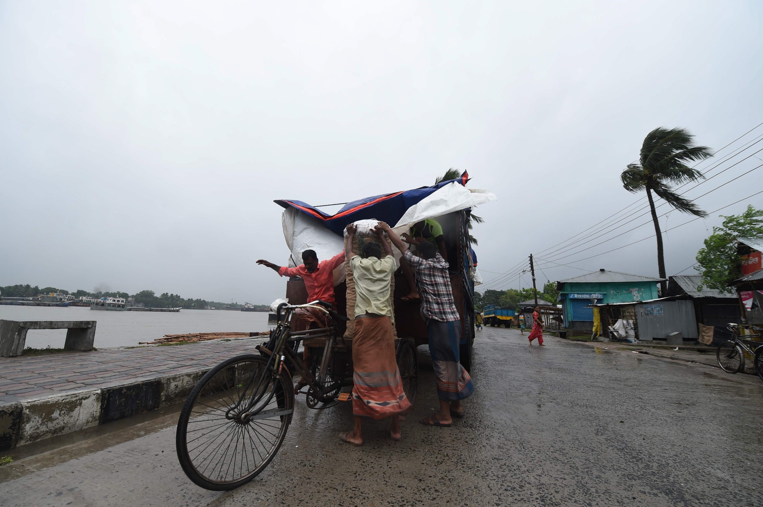 TOPSHOT - Workers unload goods from a truck ahead of the expected landfall of cyclone Amphan, in Khulna on May 20, 2020. - Several million people were taking shelter and praying for the best on Wednesday as the Bay of Bengal's fiercest cyclone in decades roared towards Bangladesh and eastern India, with forecasts of a potentially devastating and deadly storm surge. Authorities have scrambled to evacuate low lying areas in the path of Amphan, which is only the second 