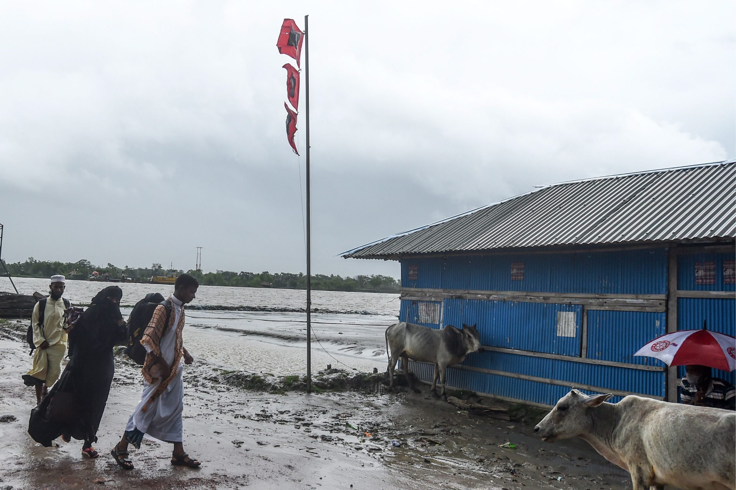 Residents walk past a great danger signal 10 flag (C) ahead of the expected landfall of cyclone Amphan, in Dacope of Khulna district on May 20, 2020. - Several million people were taking shelter and praying for the best on Wednesday as the Bay of Bengal's fiercest cyclone in decades roared towards Bangladesh and eastern India, with forecasts of a potentially devastating and deadly storm surge. Authorities have scrambled to evacuate low lying areas in the path of Amphan, which is only the second 