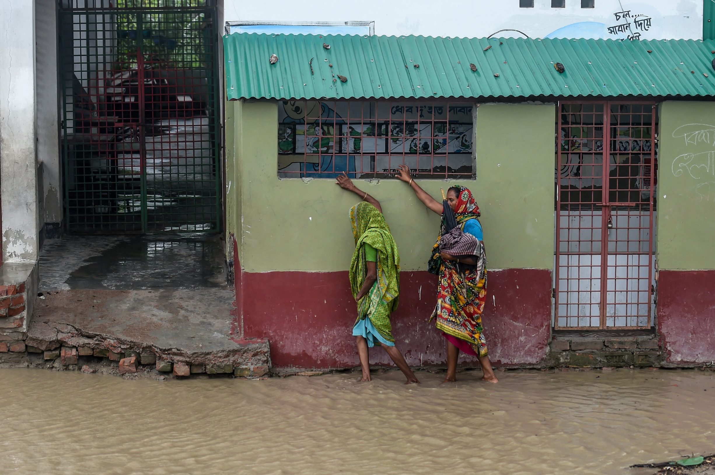 Residents walk along a house on a flooded street heading to a shelter ahead of the expected landfall of cyclone Amphan, in Dacope of Khulna district on May 20, 2020. - Several million people were taking shelter and praying for the best on Wednesday as the Bay of Bengal's fiercest cyclone in decades roared towards Bangladesh and eastern India, with forecasts of a potentially devastating and deadly storm surge. Authorities have scrambled to evacuate low lying areas in the path of Amphan, which is only the second 