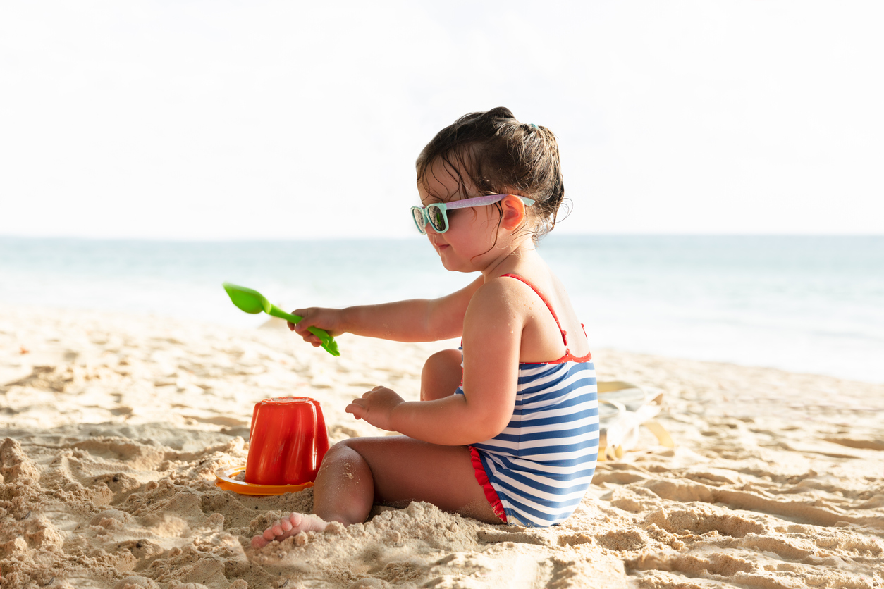 Side View Of A Little Girl Building Sand Castle With Plastic Bucket On Beach