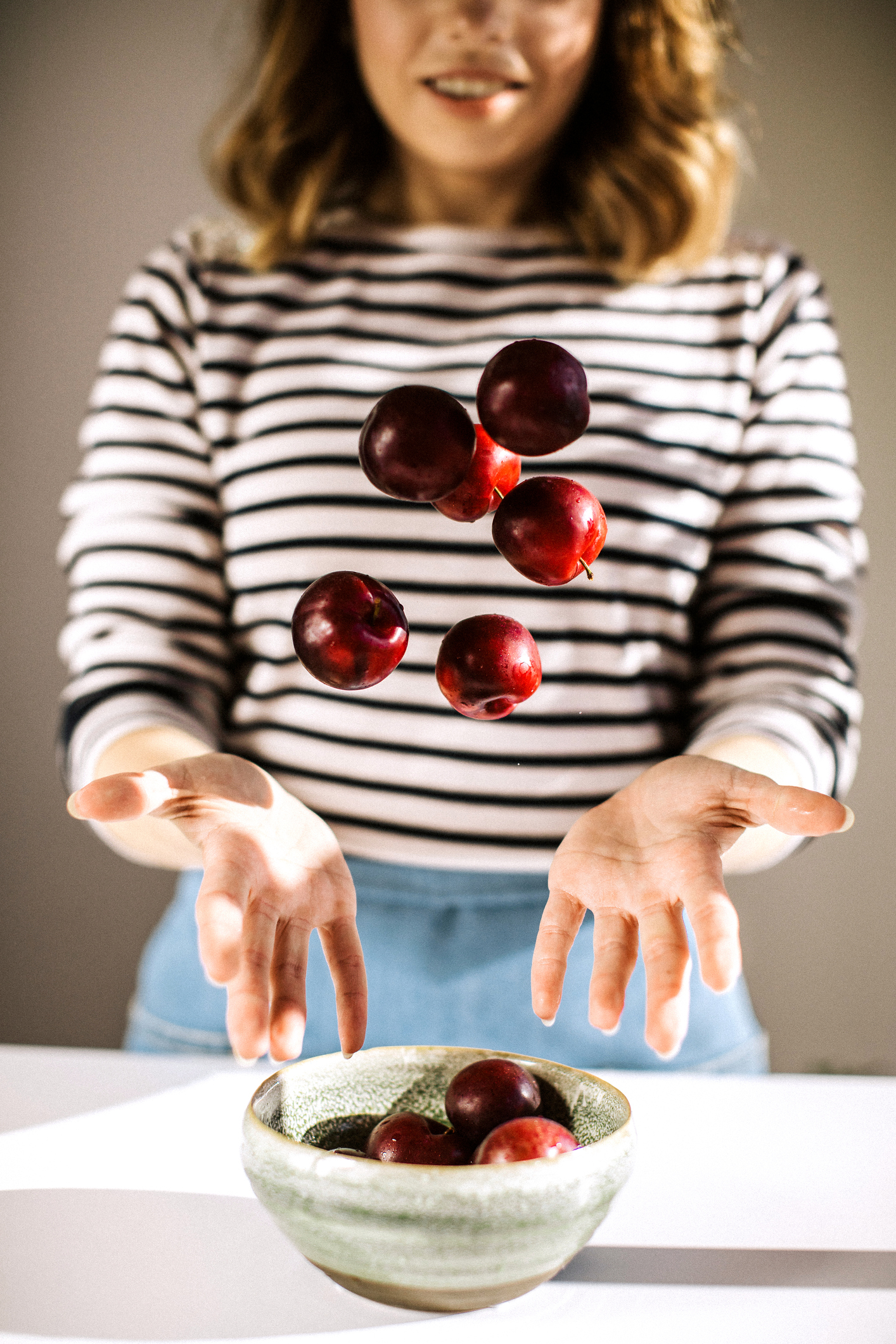 Smiling woman throwing red plums from bowl in the kitchen