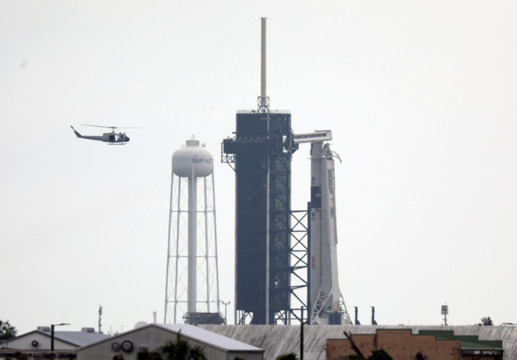 NASA security helicopter flies past launch complex 39A and the SpaceX Falcon 9 rocket with Crew Dragon vehicle on launch day at the Kennedy Space Center in Florida on May 26, 2020. - A new era in space begins Wednesday with the launch by SpaceX of two NASA astronauts into space, a capability that for six decades symbolized the power of a handful of states, and which the United States itself had been deprived of for nine years.If the bad weather clears, at 4:33 pm (20:33 GMT) a SpaceX rocket with the new Crew Dragon capsule on top will take off from Launch Pad 39A at the Kennedy Space Center, the same from which Neil Armstrong and his Apollo crewmates left for their historic journey to the Moon. (Photo by Gregg Newton / Gregg Newton / AFP)