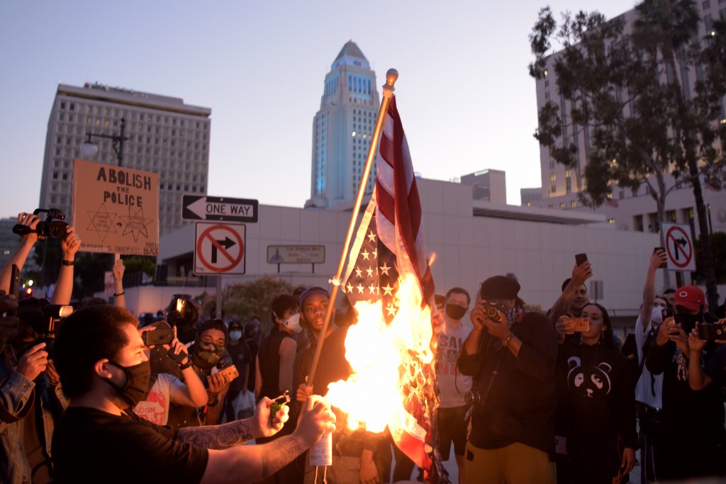 A man burns an upsidedown US flag as protesters gather in downtown Los Angeles on May 27, 2020 to demonstrate after George Floyd, an unarmed black man, died while being arrested by a police officer in Minneapolis who pinned him to the ground with his knee. - Outrage has grown across the country at Floyd's death on May 25, fuelled in part by bystander cellphone video which shows him, handcuffed and in the custody of four white police officers, on the ground while one presses his knee into the victim's neck. (Photo by Agustin PAULLIER / AFP)