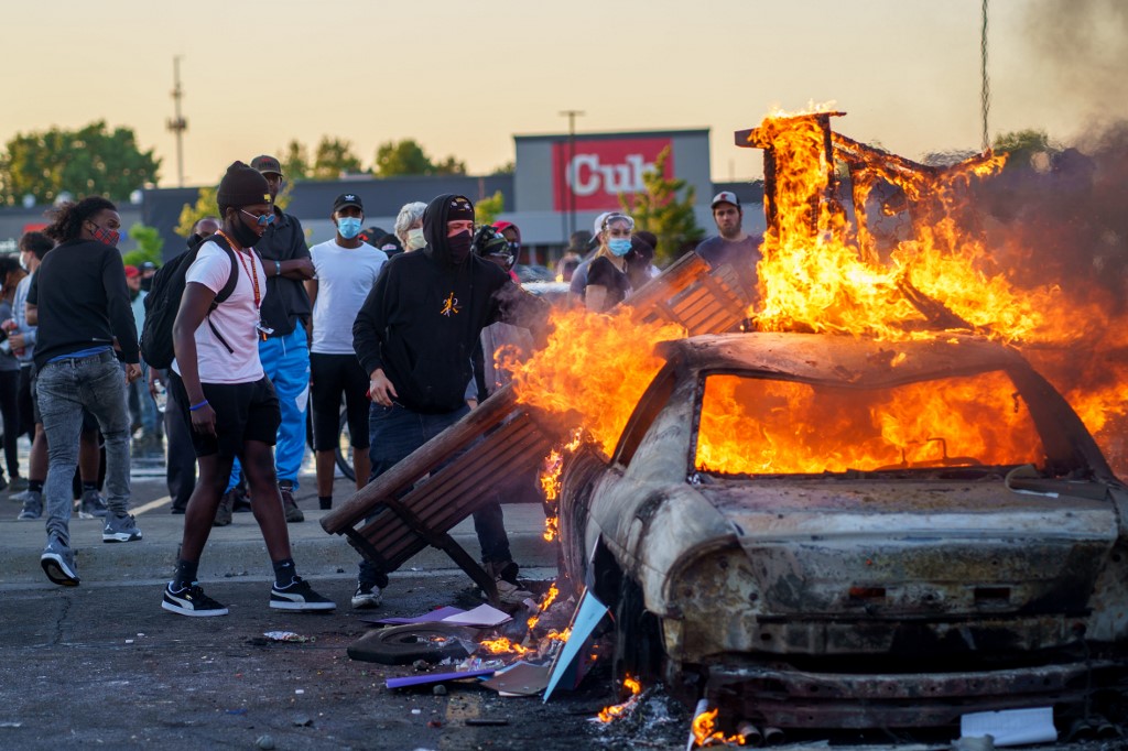 Protesters throw objects onto a burning car outside a Target store near the Third Police Precinct on May 28, 2020 in Minneapolis, Minnesota, during a demonstration over the death of George Floyd, an unarmed black man, who died after a police officer kneeled on his neck for several minutes. - Authorities in Minneapolis and its sister city St. Paul got reinforcements from the National Guard on May 28 as they girded for fresh protests and violence over the shocking police killing of a handcuffed black man. Three days after a policeman was filmed holding his knee to George Floyd's neck for more than five minutes until he went limp, outrage continued to spread over the latest example of police mistreatment of African Americans. (Photo by kerem yucel / AFP)