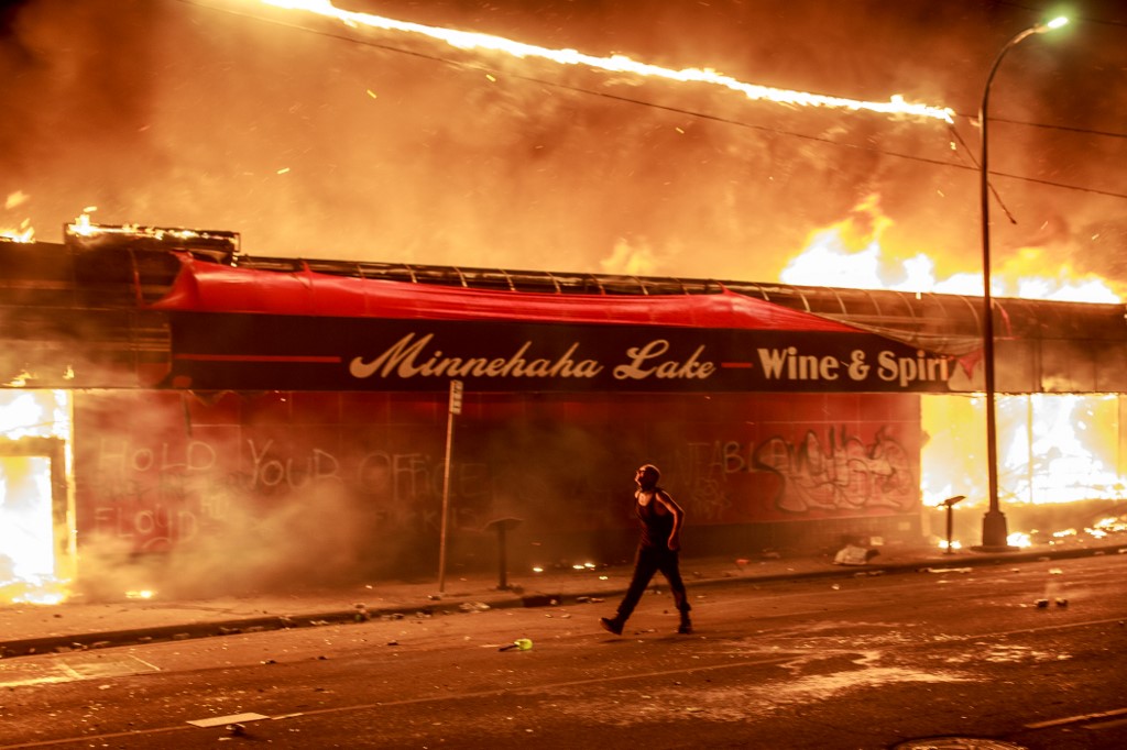 A man walks past a liquor store in flames near the Third Police Precinct on May 28, 2020 in Minneapolis, Minnesota, during a protest over the death of George Floyd, an unarmed black man, who died after a police officer kneeled on his neck for several minutes. - A police precinct in Minnesota went up in flames late on May 28 in a third day of demonstrations as the so-called Twin Cities of Minneapolis and St. Paul seethed over the shocking police killing of a handcuffed black man. The precinct, which police had abandoned, burned after a group of protesters pushed through barriers around the building, breaking windows and chanting slogans. A much larger crowd demonstrated as the building went up in flames. (Photo by Kerem Yucel / AFP)