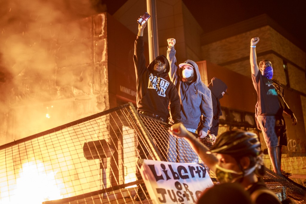Protesters hold up their fists as flames rise behind them in front of the Third Police Precinct on May 28, 2020 in Minneapolis, Minnesota, during a protest over the death of George Floyd, an unarmed black man, who died after a police officer kneeled on his neck for several minutes. - A police precinct in Minnesota went up in flames late on May 28 in a third day of demonstrations as the so-called Twin Cities of Minneapolis and St. Paul seethed over the shocking police killing of a handcuffed black man. The precinct, which police had abandoned, burned after a group of protesters pushed through barriers around the building, breaking windows and chanting slogans. A much larger crowd demonstrated as the building went up in flames. (Photo by Kerem Yucel / AFP)