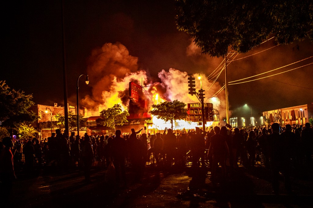 Protesters gather around a liquor store in flames near the Third Police Precinct on May 28, 2020 in Minneapolis, Minnesota, during a protest over the death of George Floyd, an unarmed black man, who died after a police officer kneeled on his neck for several minutes. - A police precinct in Minnesota went up in flames late on May 28 in a third day of demonstrations as the so-called Twin Cities of Minneapolis and St. Paul seethed over the shocking police killing of a handcuffed black man. The precinct, which police had abandoned, burned after a group of protesters pushed through barriers around the building, breaking windows and chanting slogans. A much larger crowd demonstrated as the building went up in flames. (Photo by Kerem Yucel / AFP)
