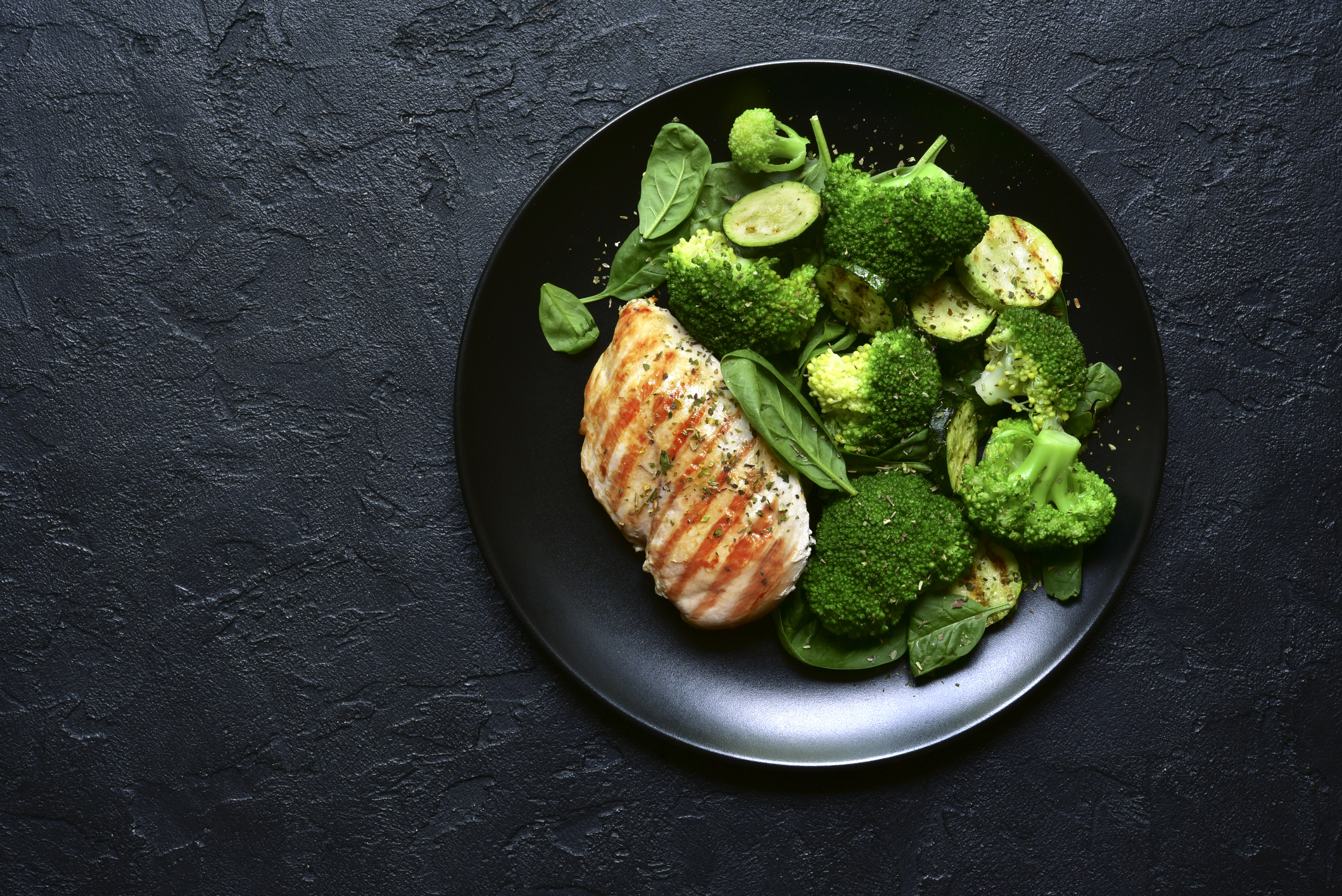 Grilled chicken fillet with green vegetable salad on a black slate, stone or concrete background.Top view with copy space.