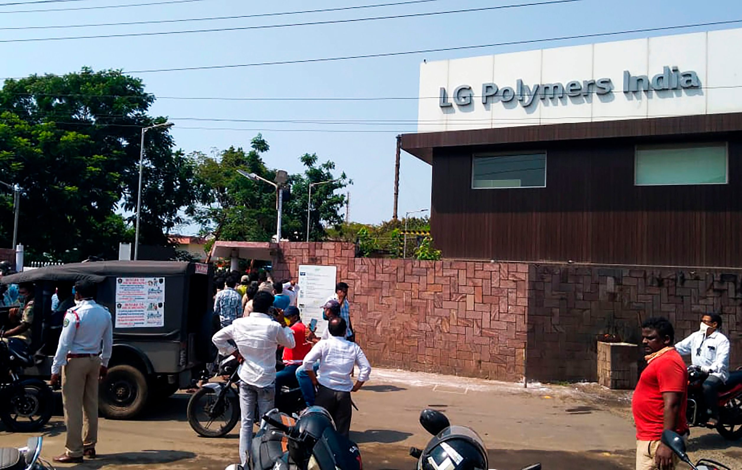 Policemen stand guard as people gather in front of a LG Polymers plant following a gas leak incident in Visakhapatnam on May 7, 2020. - At least five people have been killed and several hundred hospitalised after a gas leak at a chemicals plant on the east coast of India, police said on May 7. They said that the gas had leaked out of two 5,000-tonne tanks that had been unattended due to India's coronavirus lockdown in place since late March. (Photo by - / AFP)