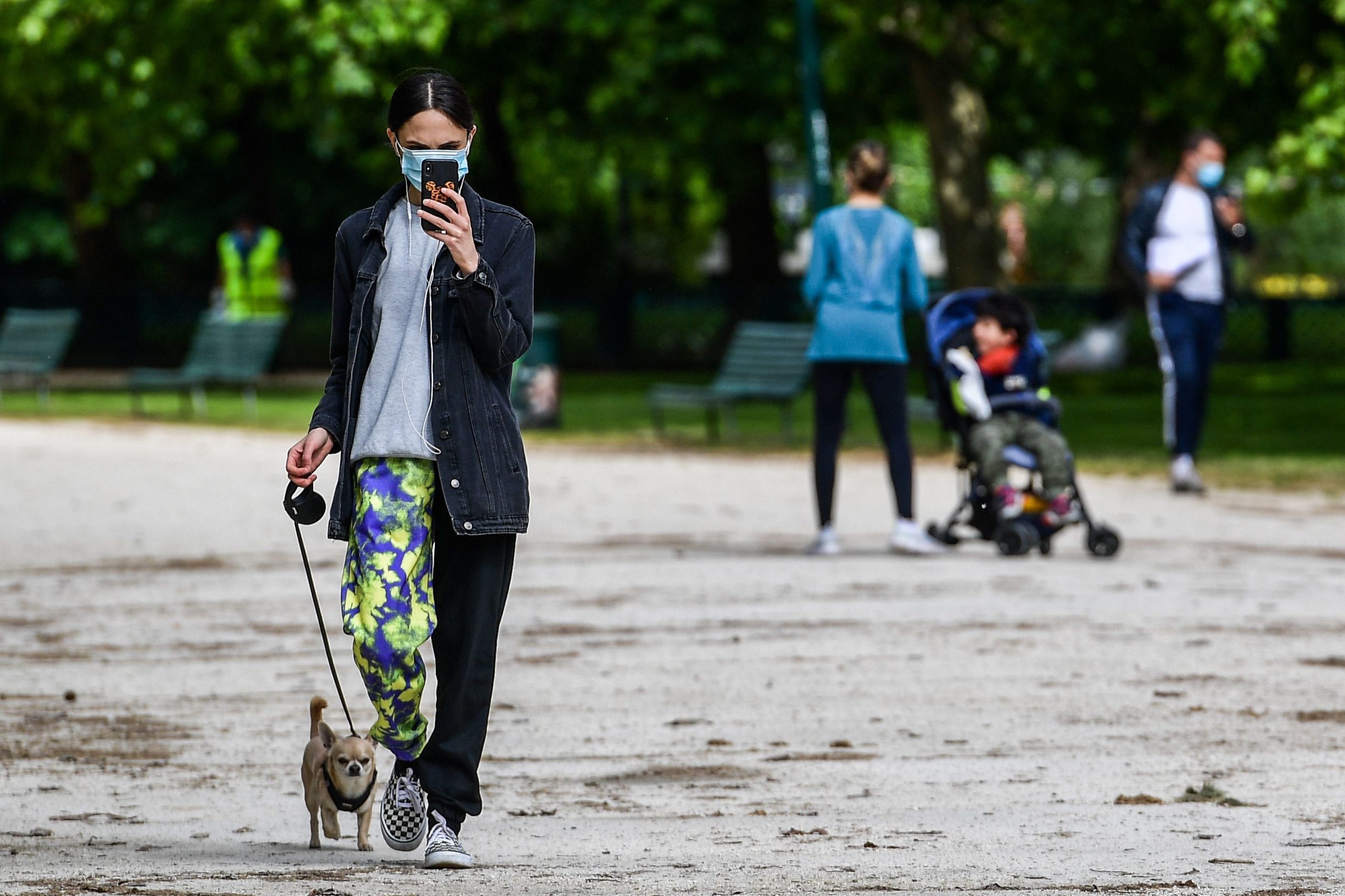 A woman checks her smartphone as she walks her dog in the Parco Sempione park on May 4, 2020 in Milan as Italy starts to ease its lockdown, during the country's lockdown aimed at curbing the spread of the COVID-19 infection, caused by the novel coronavirus. - Stir-crazy Italians will be free to stroll and visit relatives for the first time in nine weeks on May 4, 2020 as Europe's hardest-hit country eases back the world's longest nationwide coronavirus lockdown. (Photo by Miguel MEDINA / AFP)