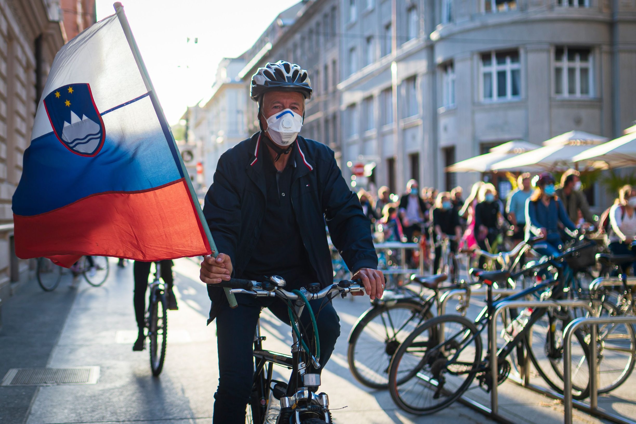 A Slovenian citizen, wearing protective masks, holds a Slovenian flag as he and others ride their bikes as they block the centre of capital Ljubljana to protest against the centre-right government, accusing it of corruption and of using the novel coronavirus crisis to restrict freedom on May 8, 2020 amid the COVID-19 outbreak, caused by the novel coronavirus. (Photo by Jure Makovec / AFP)