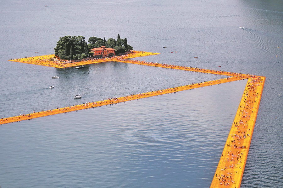 (FILES) In this file photo taken on June 18, 2016 people walk on the monumental installation entitled 'The Floating Piers' created by artist Christo Vladimirov Javacheff on Iseo Lake, in northern Italy. - The artist known as Christo, who made his name transforming landmarks such as Germany's Reichstag by covering them with reams of cloth, died on May 31, 2020 aged 84, his official Facebook page announced. Christo Vladimirov Javacheff died of natural causes at his home in New York City, the statement said. The Bulgarian-born artist worked in collaboration with his wife of 51 years Jeanne-Claude until her death in 2009. (Photo by MARCO BERTORELLO / AFP) / RESTRICTED TO EDITORIAL USE - MANDATORY MENTION OF THE ARTIST UPON PUBLICATION - TO ILLUSTRATE THE EVENT AS SPECIFIED IN THE CAPTION