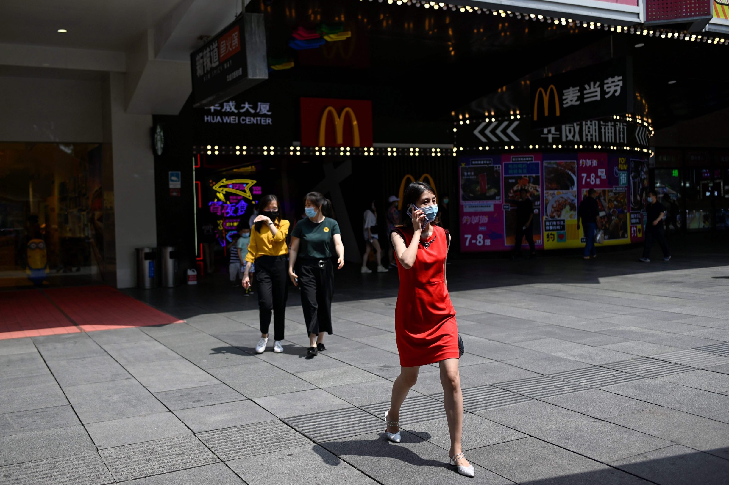 A woman wearing a face mask uses her mobile phone while walking out of a mall in Beijing on June 10, 2020. (Photo by WANG Zhao / AFP)