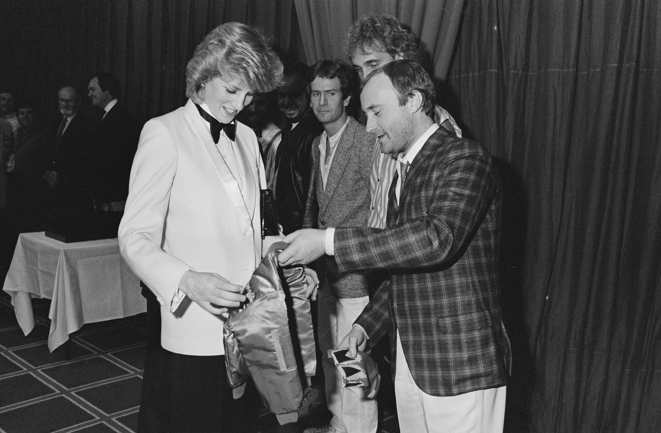 Diana, Princess of Wales (1961 - 1997) accepts a jacket with an embroidered gold crown for Prince William from British singer and drummer Phil Collins of rock band Genesis, before the band gave a Royal charity concert at the National Exhibition Centre, Birmingham, UK, 2nd March 1984. (Photo by Steve Wood/Daily Express/Hulton Archive/Getty Images)
