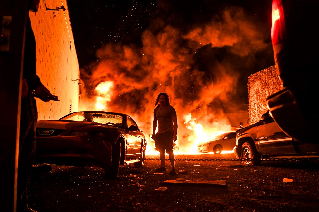 A man tries to toe away a car in a safe zone as the other car catches fire in a local parking garage on May 29, 2020 in Minneapolis, Minnesota, during a protest over the death of George Floyd, an unarmed black man, who died after a police officer kneeled on his neck for several minutes. - The Minneapolis police officer accused of killing a handcuffed African-American man was charged with murder on May 29, but the move failed to quell surging anger as tense protests erupted in cities across the nation. (Photo by CHANDAN KHANNA / AFP)